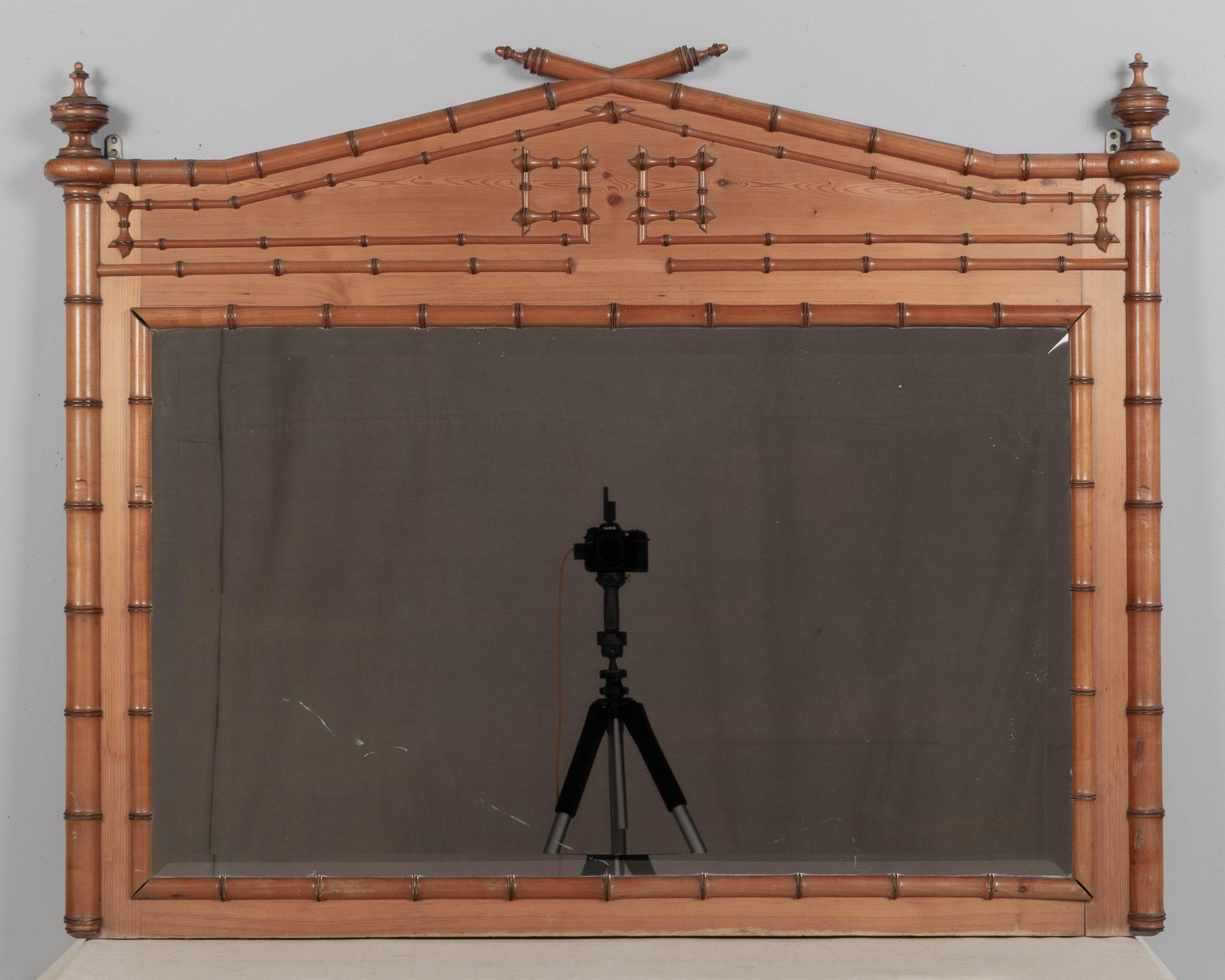 A 19th century French faux bamboo beveled wall mirror with triangular crown pediment and turned finials. Made of pine with solid cherry faux bamboo details. Waxed patina. Good quality and craftsmanship. Mirror has light scratches and finials have