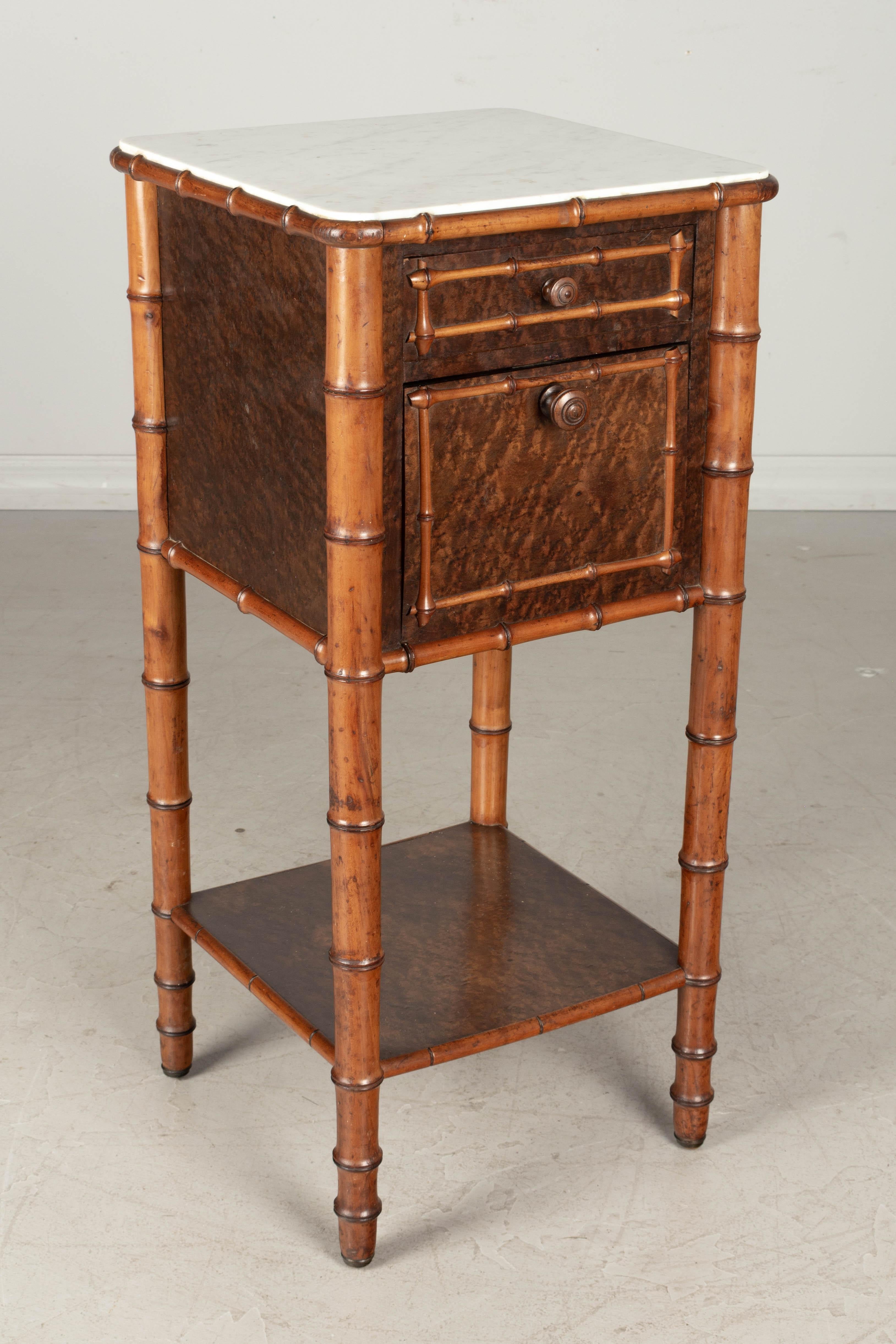 A 19th century French faux bamboo bedside table, or nightstand, made of cherry and dark stained birdseye maple. Dovetailed drawer and a door that hinges open to reveal an interior compartment, once used to store a chamber pot. Turned knobs and legs