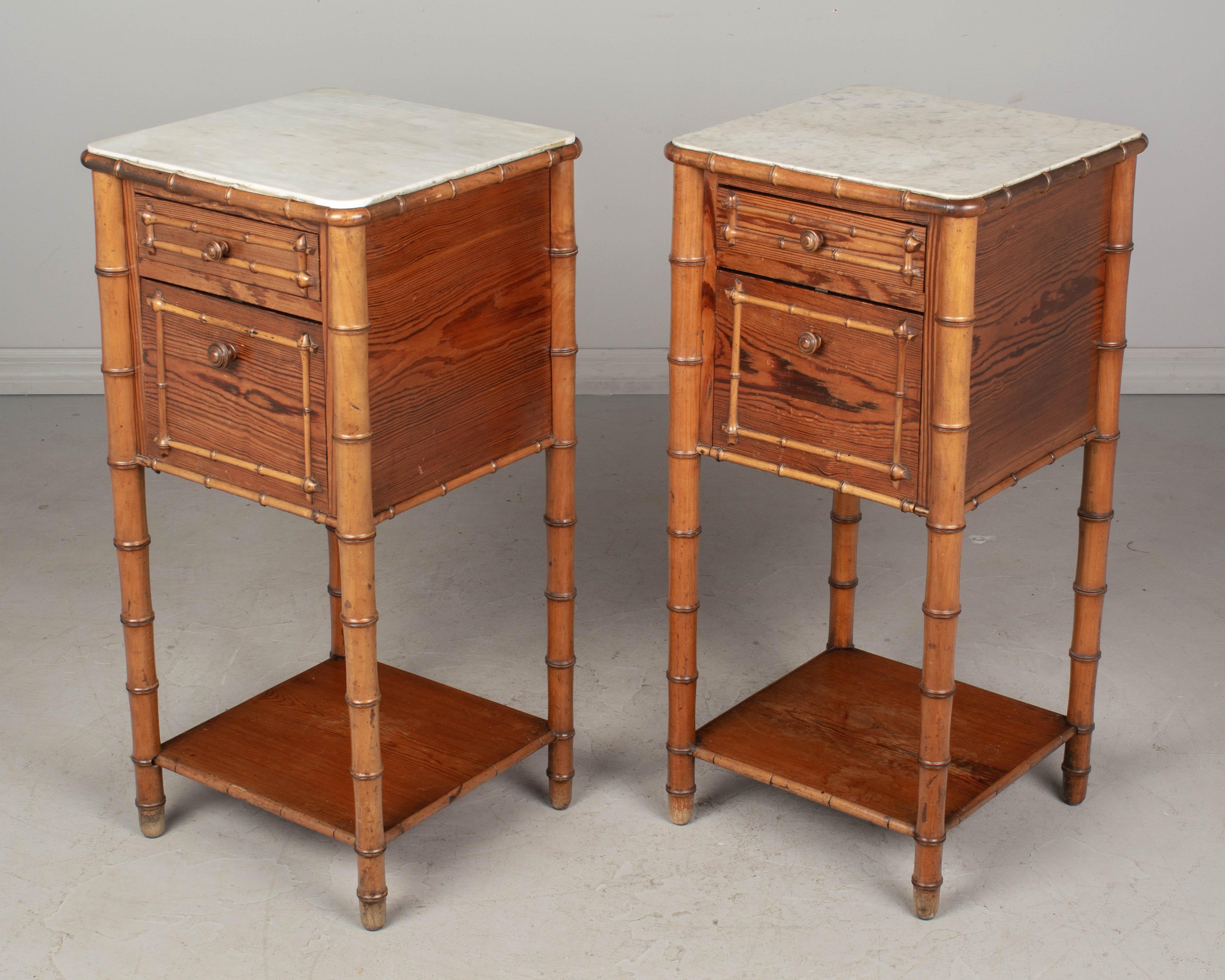 A pair of 19th century French faux bamboo bedside tables, or nightstands, made of cherry and pine. Each with a dovetailed drawer and a door that hinges open to reveal a marble lined interior compartment, once used to store a chamber pot. Turned