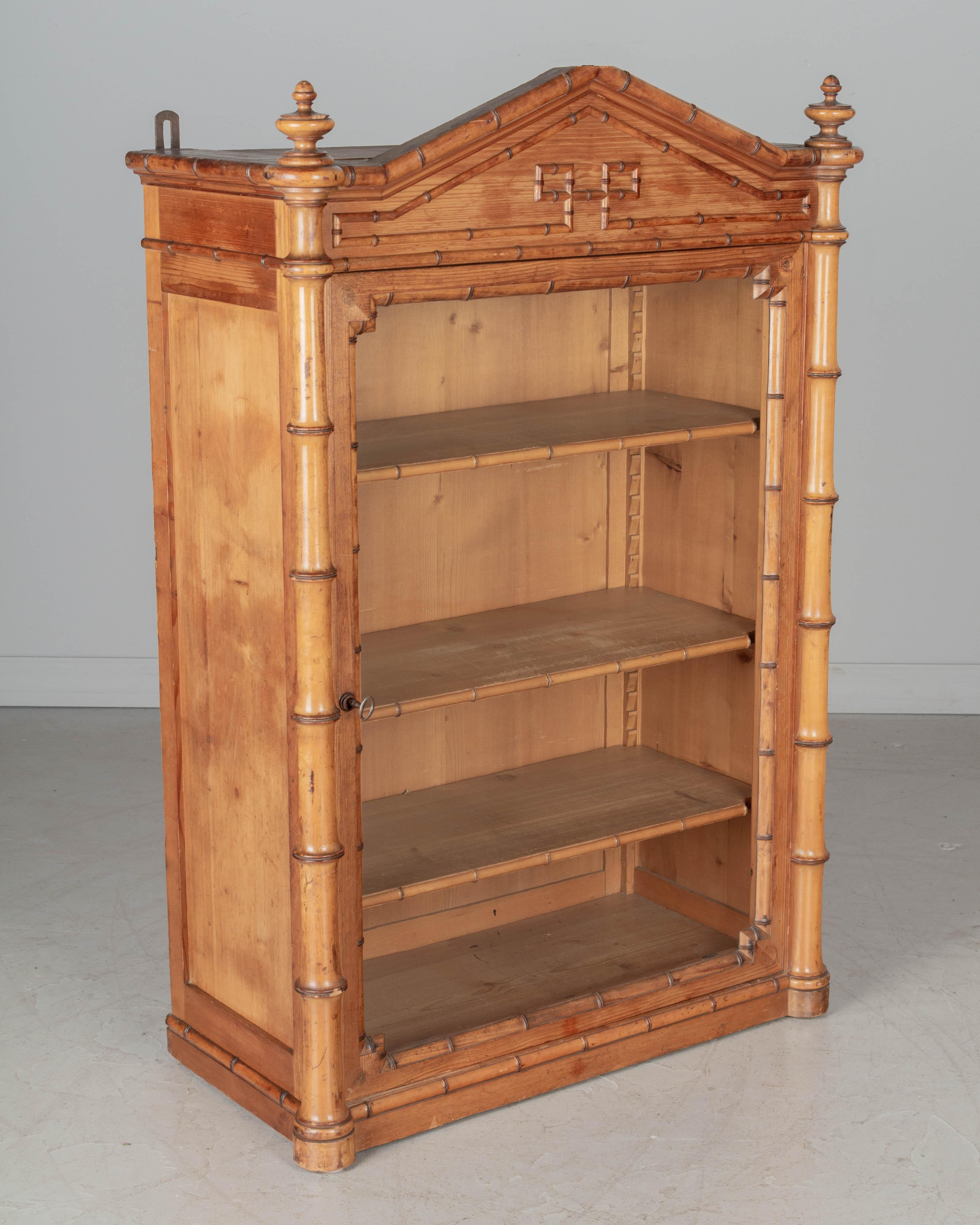 A 19th Century French faux bamboo vitrine or wall cabinet made of pitch pine with turned cherry wood details and finials. Glass paned door with three adjustable shelves. Brackets on the back to hang on the wall. All original. In very good condition.