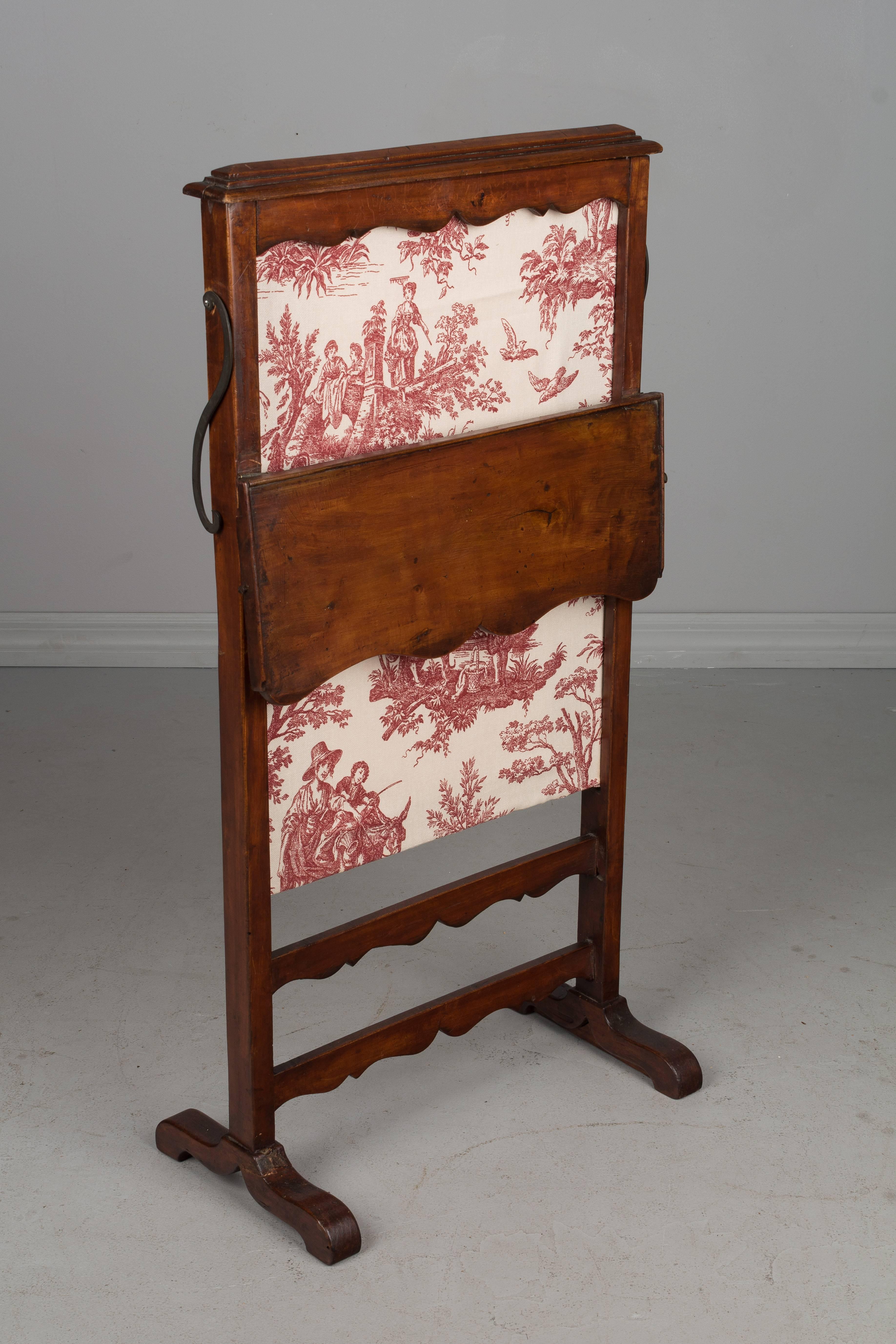 A 19th century country French fire screen made of pear wood with a small hinged tray and sliding panel. Replaced toile fabric. Prior restoration on legs. Please refer to photos for more details. We have a large selection of French antiques at