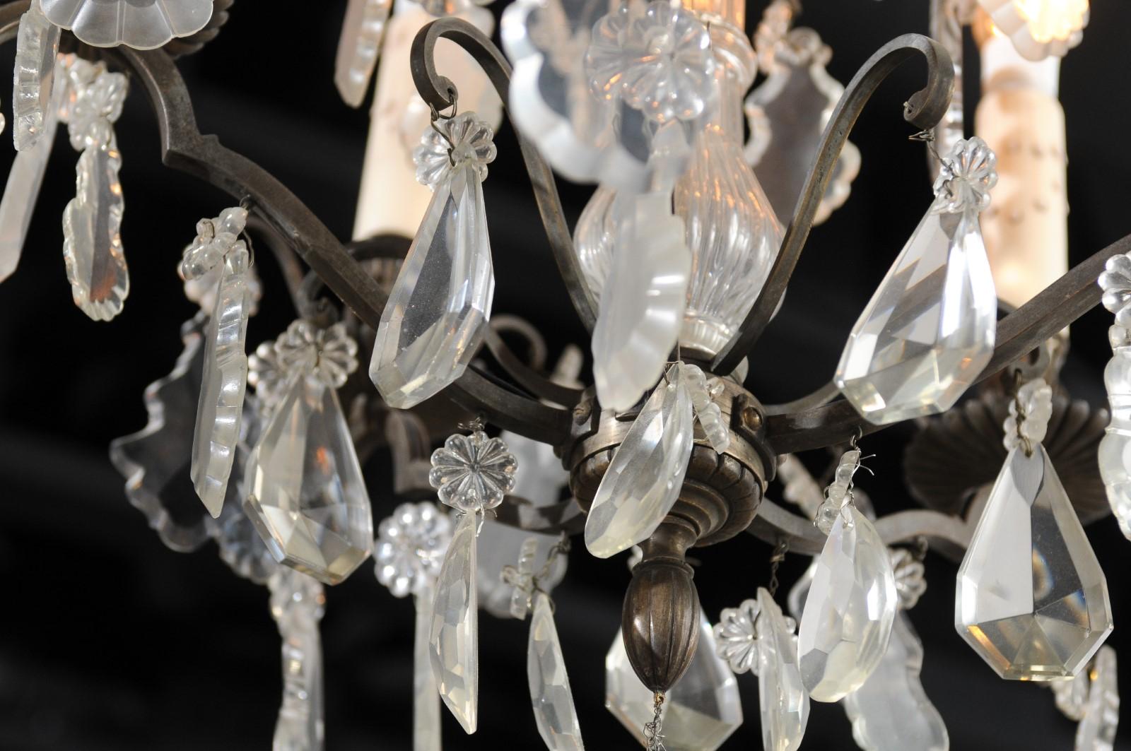 A French five-light iron and crystal chandelier from the 19th century, with pendeloques, rosettes and flower bobeches. Created in France during the 19th century, this chandelier features an iron armature with scrolling accents and central crystal