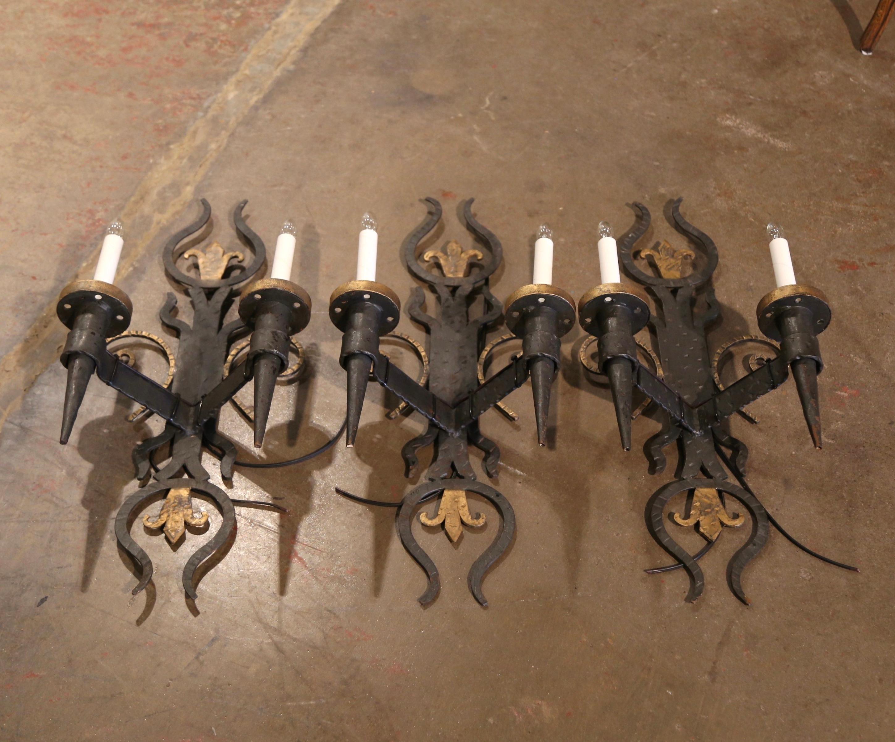 Decorate a hallway or entryway with this set of antique wall torcheres. Crafted in France, circa 1890, the fixtures are built of forged and hammered iron with scroll decor and further embellished with a Fleur-de-Lis motif at the top and bottom. Each