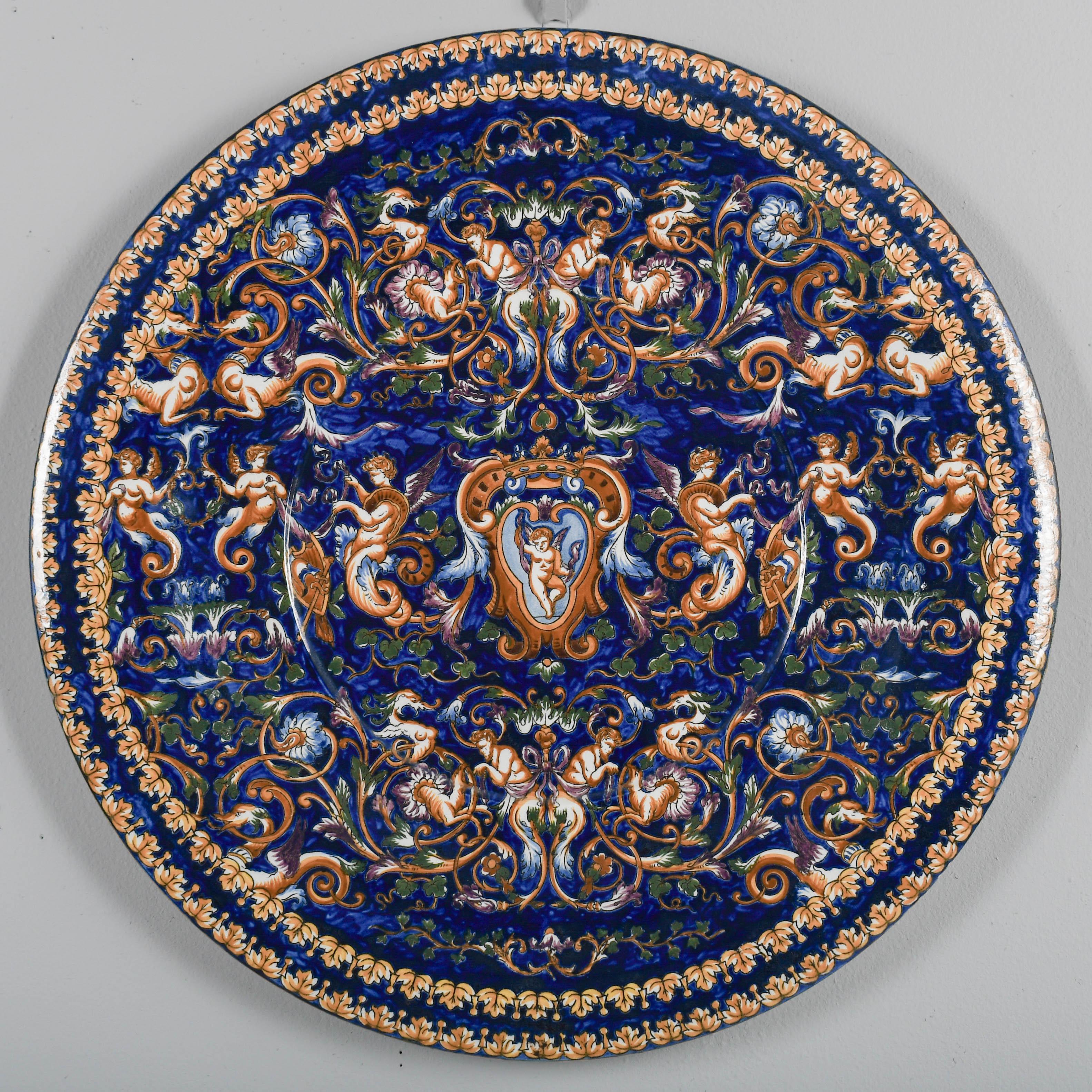 Caricatore decorativo o ciotola bassa in faience francese del XIX secolo, dipinto a mano in arancione, verde e azzurro su fondo blu cobalto con immagini in stile rinascimentale, tra cui un medaglione centrale con cupido e corona, motivi allegorici,