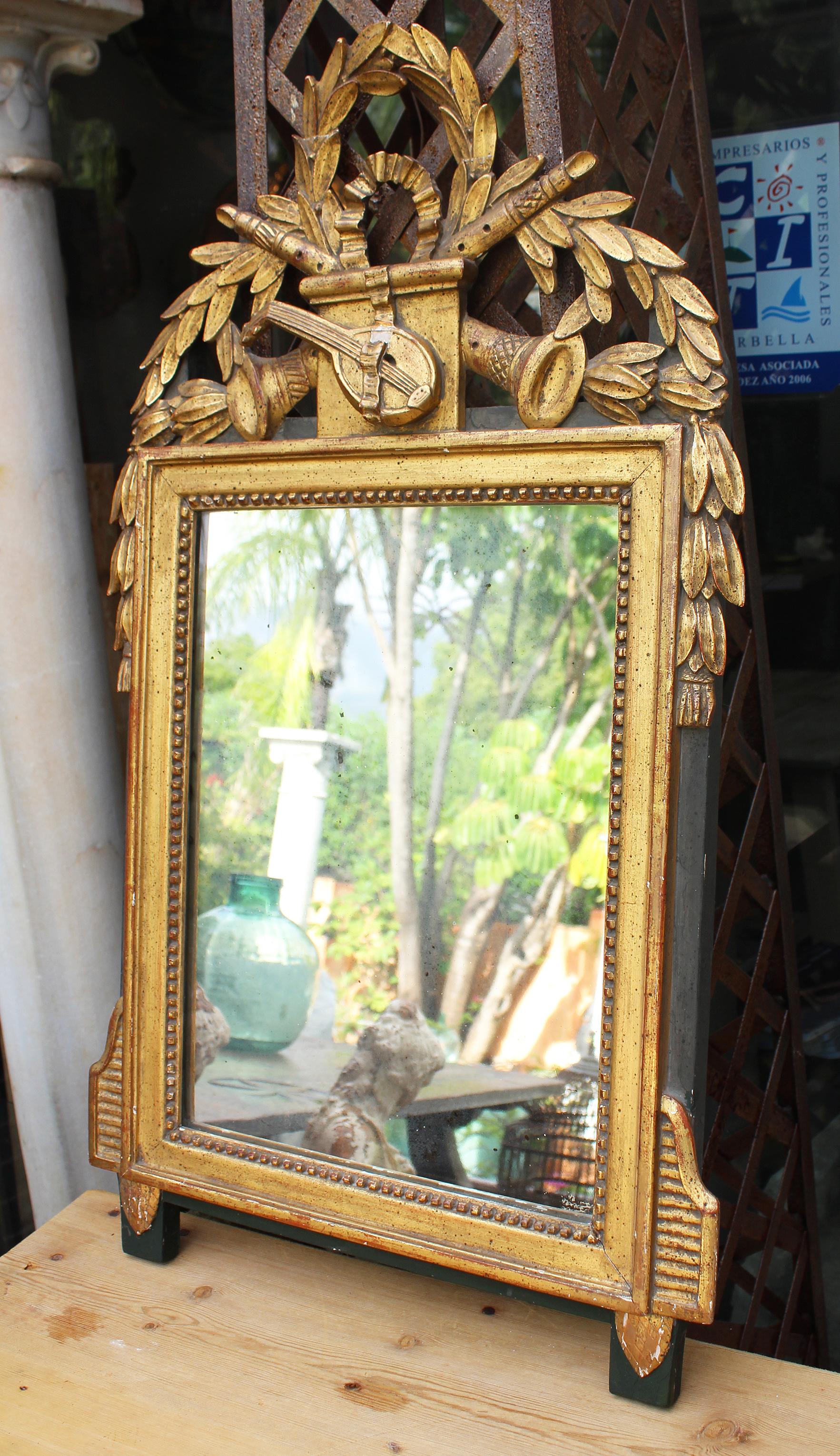19th century French gilded hand carved wooden mirror topped with a guitar, flutes and profusely decorated with bay leaf garlands.

 