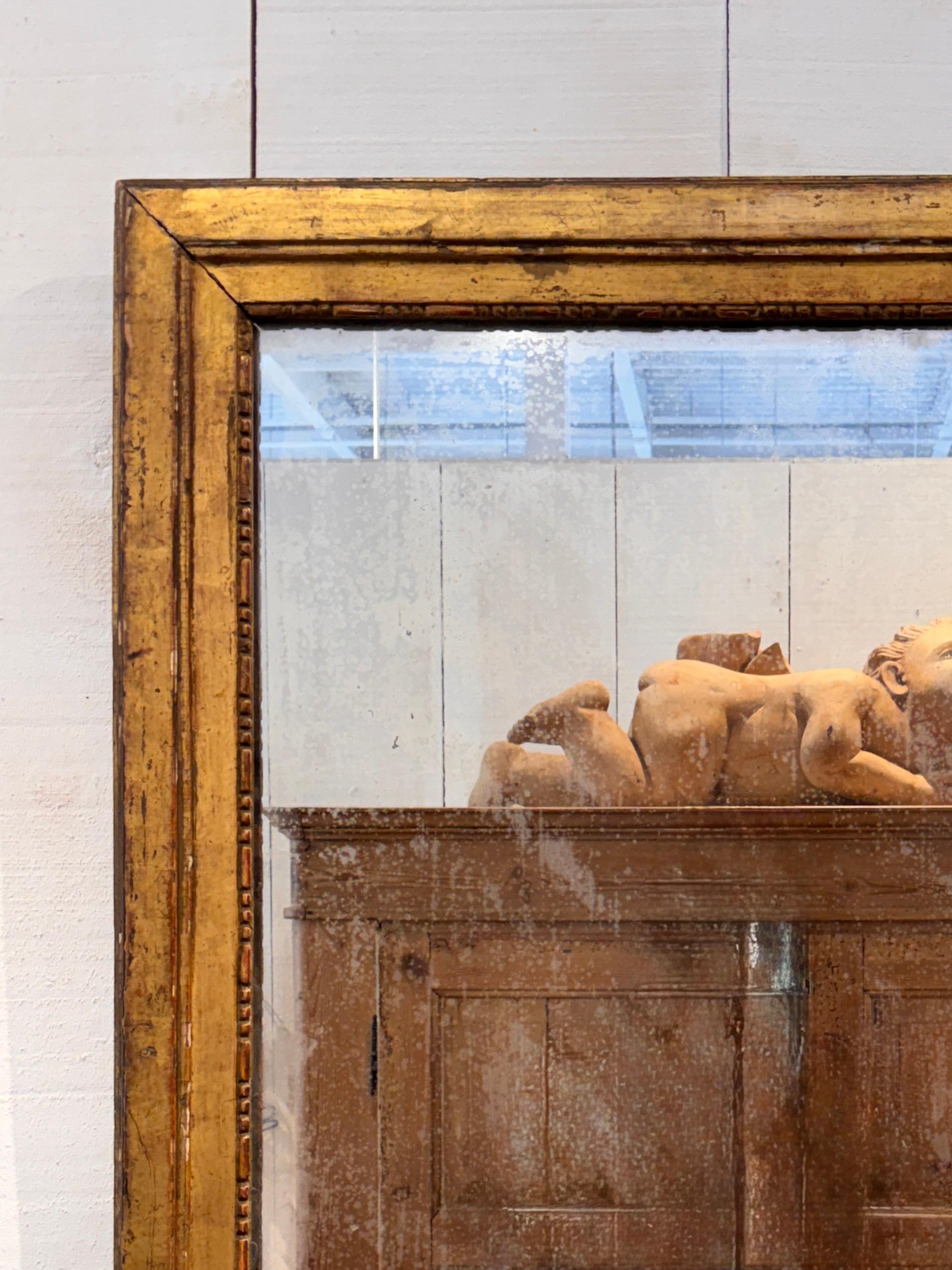 Miroir français du XIXe siècle dans un cadre orné de gesso doré de style d'époque, avec une dorure usée et un âge visible à la fois à la surface du cadre et à la plaque de miroir d'origine. L'image en gros plan montre les bords moulés et les zones