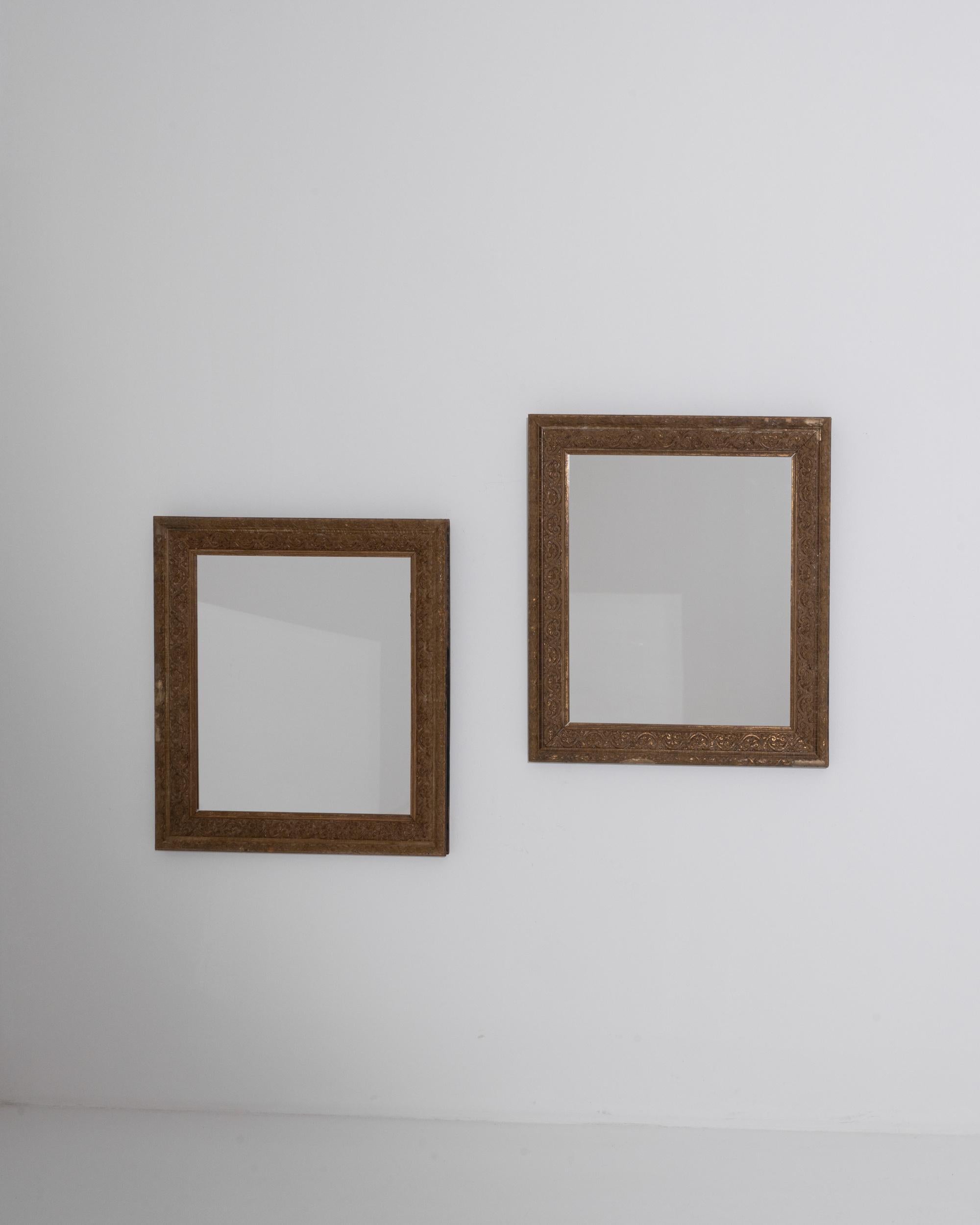 A pair of gilded wooden mirrors made in 19th century France. This pair of deceptively simple mirrors reveal a network of bustling details upon further inspection. A foliated scroll pattern wraps the border of the frames, a time-worn patina