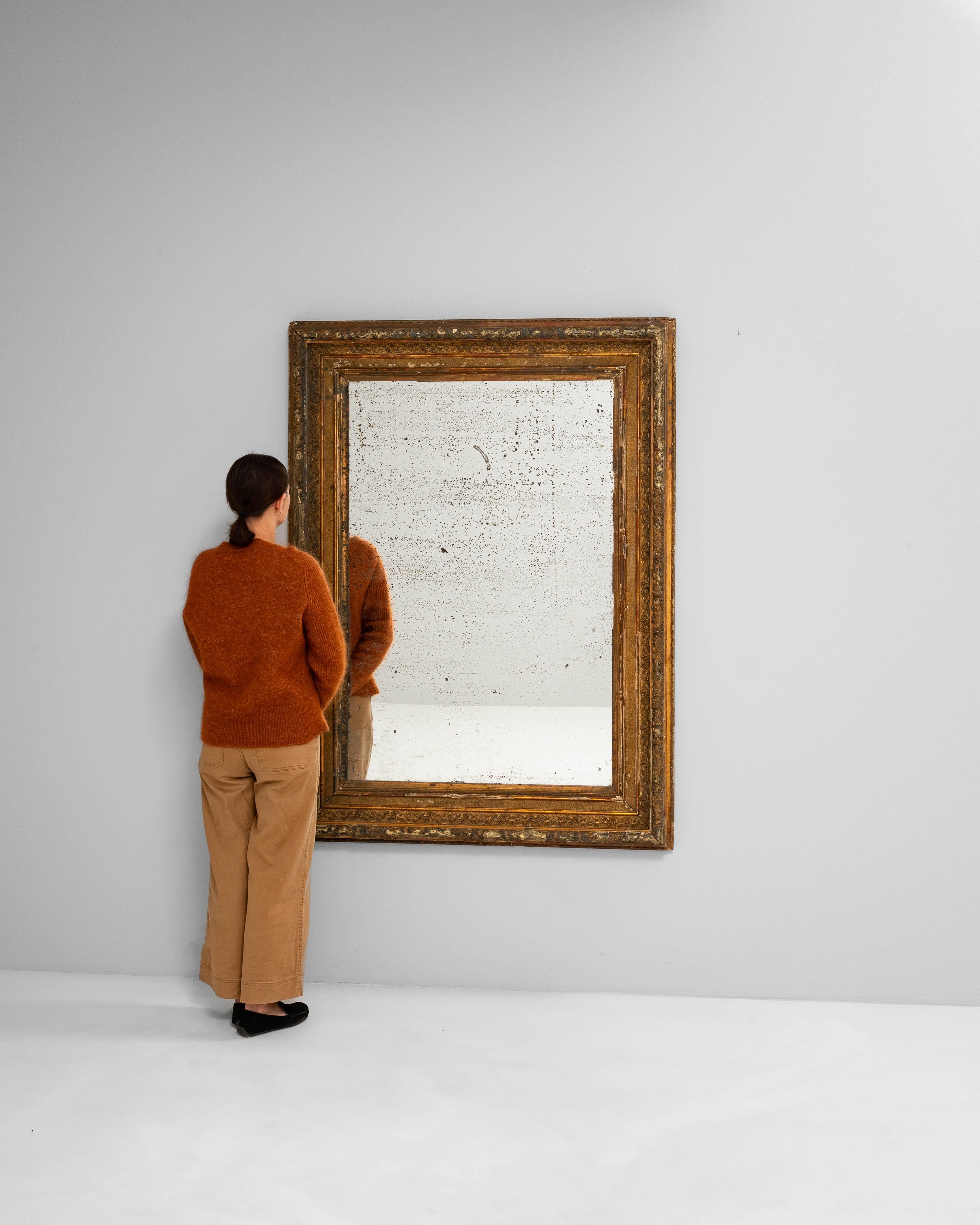 Ce miroir français du XIXe siècle se distingue par son cadre en bois doré richement sculpté, parsemé de bordures décoratives et de détails élaborés. La surface présente une patine magnifiquement vieillie avec des zones d'usure et de perte qui