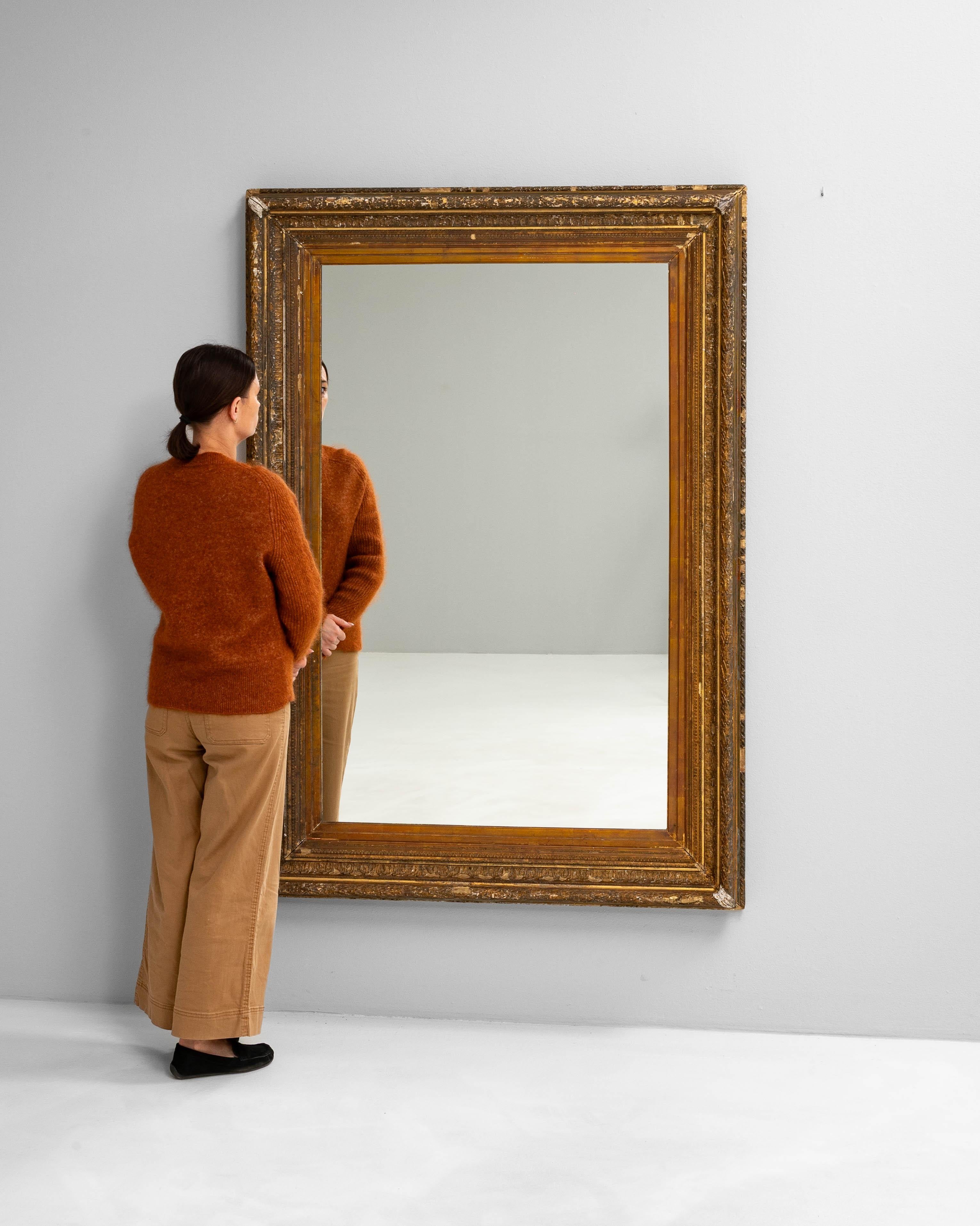 Ce miroir français du XIXe siècle est encadré de bois doré sculpté de façon complexe, mettant en valeur des moulures superposées avec un mélange harmonieux d'ornementation classique. Le cadre présente une finition usée par le temps avec des zones de