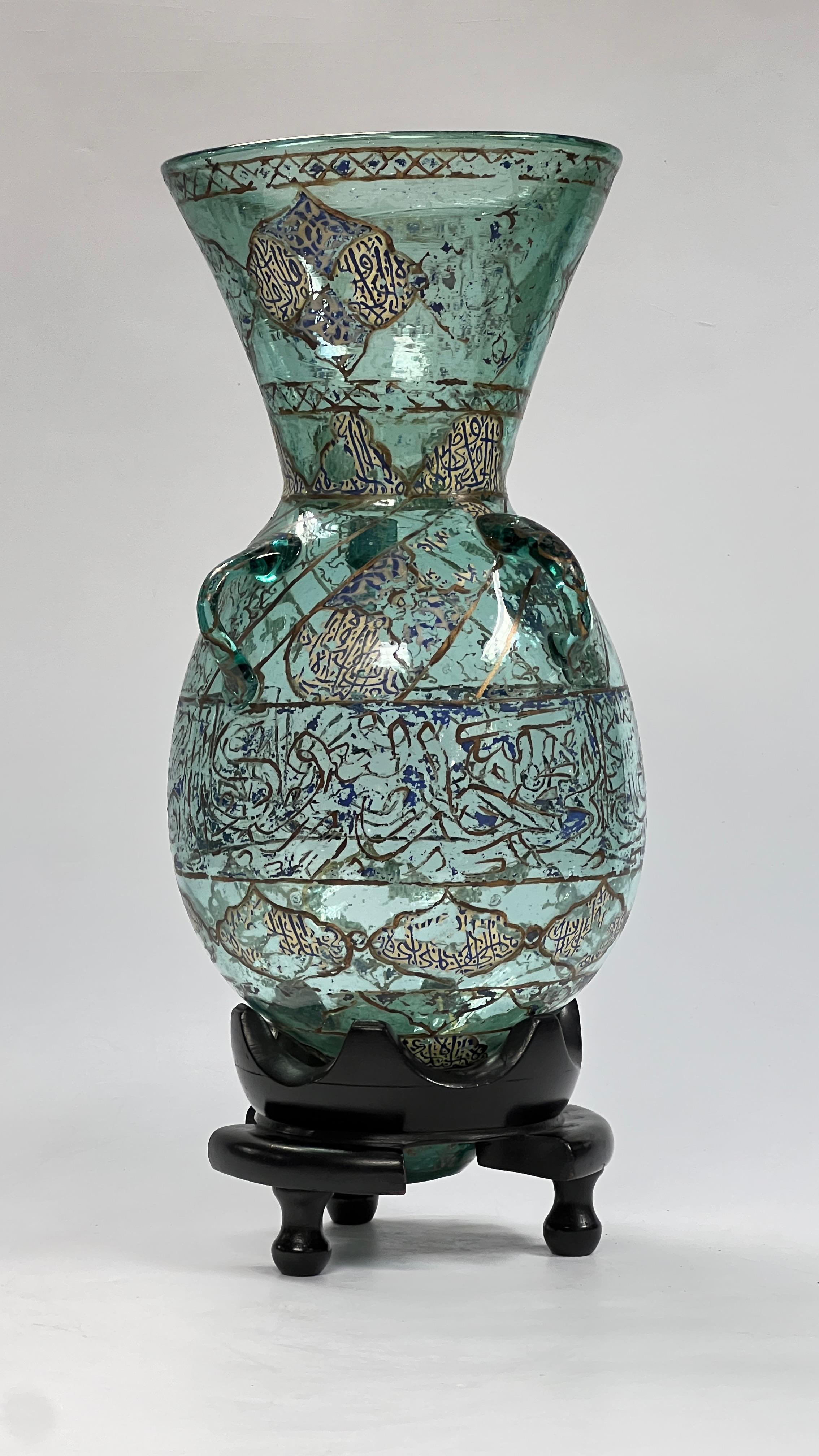Magnificent antique (19th century) French enameled and gilt turquoise glass mosque lamp decorated with gilt bands and lobes with Islamic inscriptions. With later (20th century) ebonized wooden stand.  18 by 8 inches.