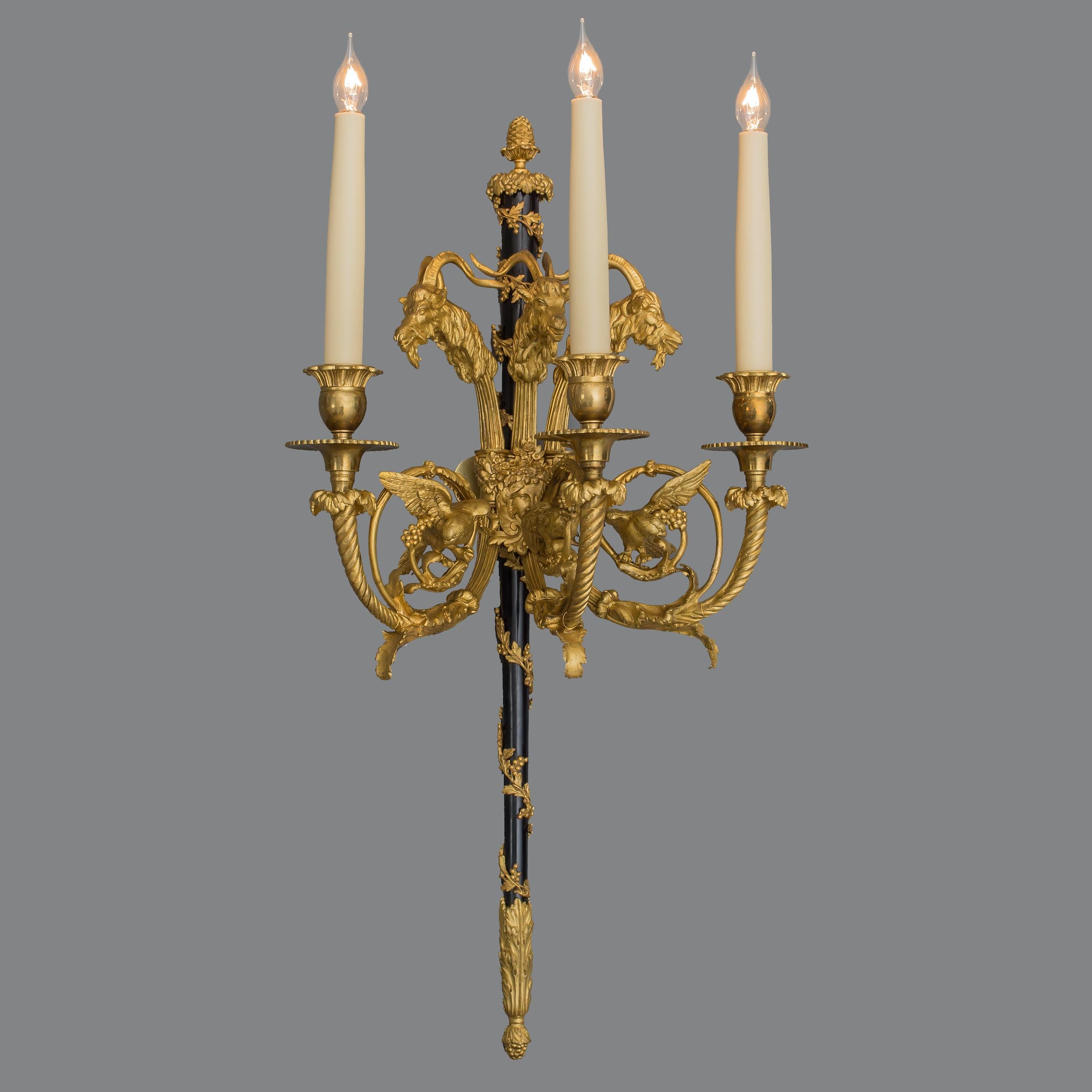 A suite of four wall appliques
In the Louis XVI Style

Constructed from gilt and patinated bronze, each applique designed around a central vine-wrapped thyrsus with acorn finial, issuing three scrolling arms of stylised acanthus, with fluttering