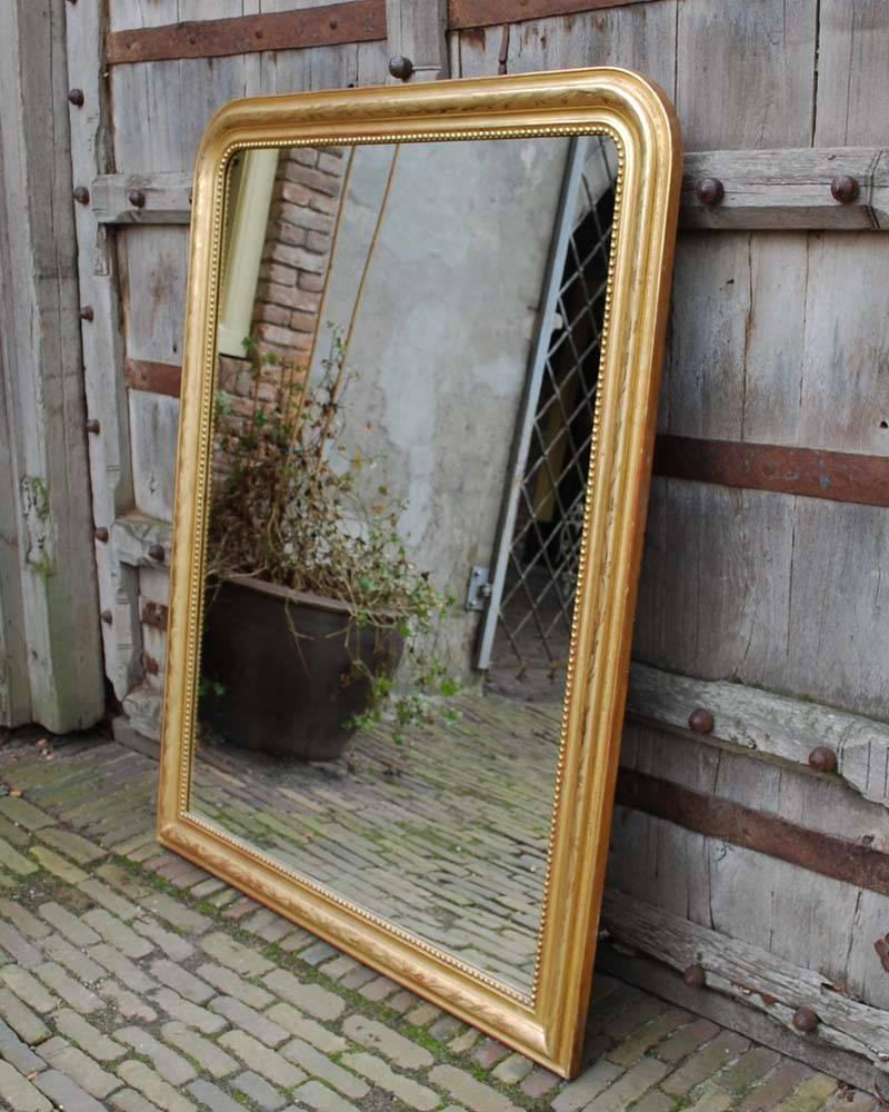 Frech gilt carved wood and plaster wall mirror with rounded corners at the top.
The frame has an internal pearl beading and floral etching on the most elevated part.
The frame has the typical gold finish. A red earth Bolus layer to polish the