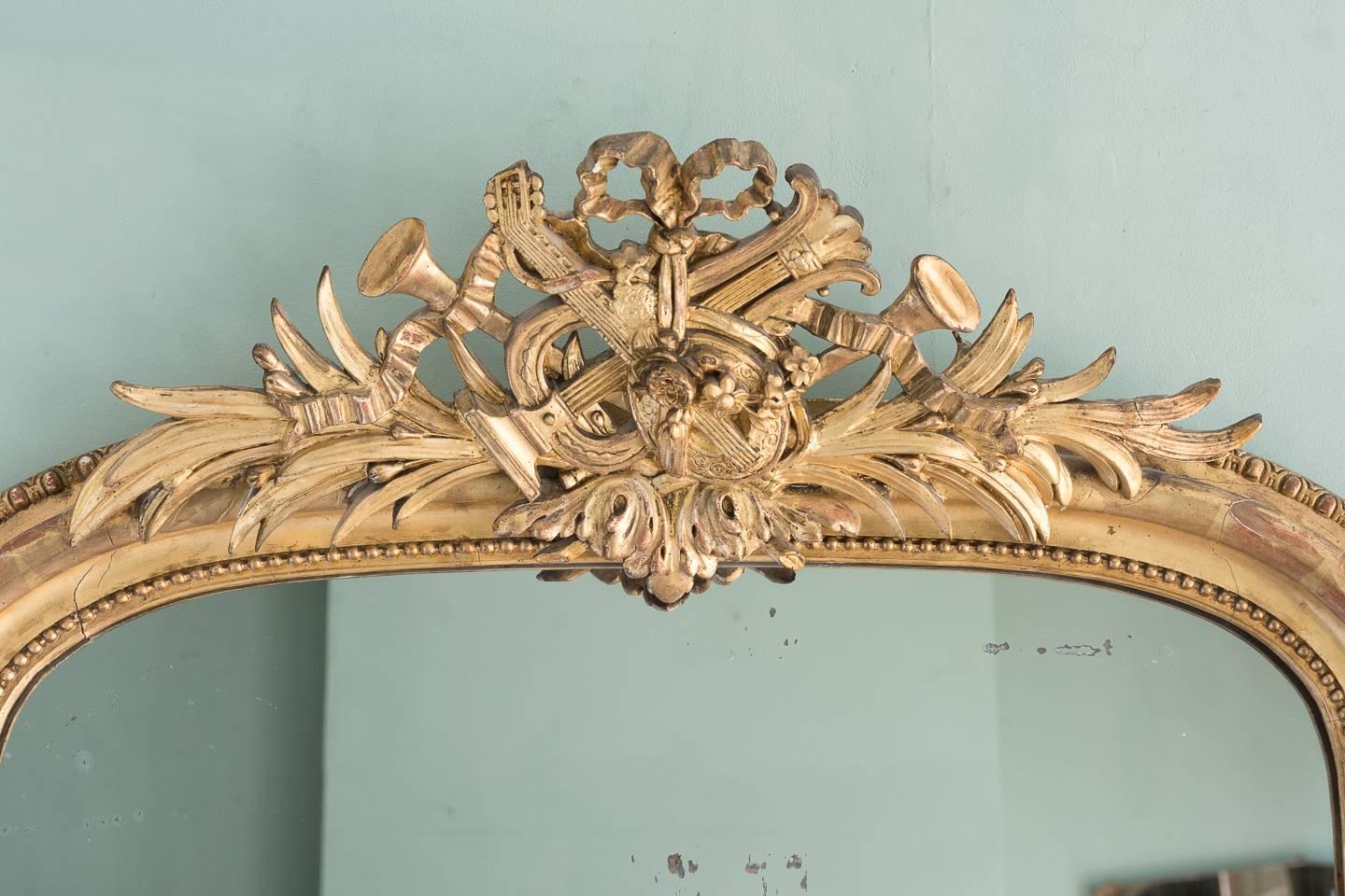 A 19th century French gilt overmantel mirror, circa 1850-1870, with cresting of ribbons and musical instruments, the arch top frame with egg and dart, bead and foliate decoration.

It could be supposed from the iconography of the cresting that this