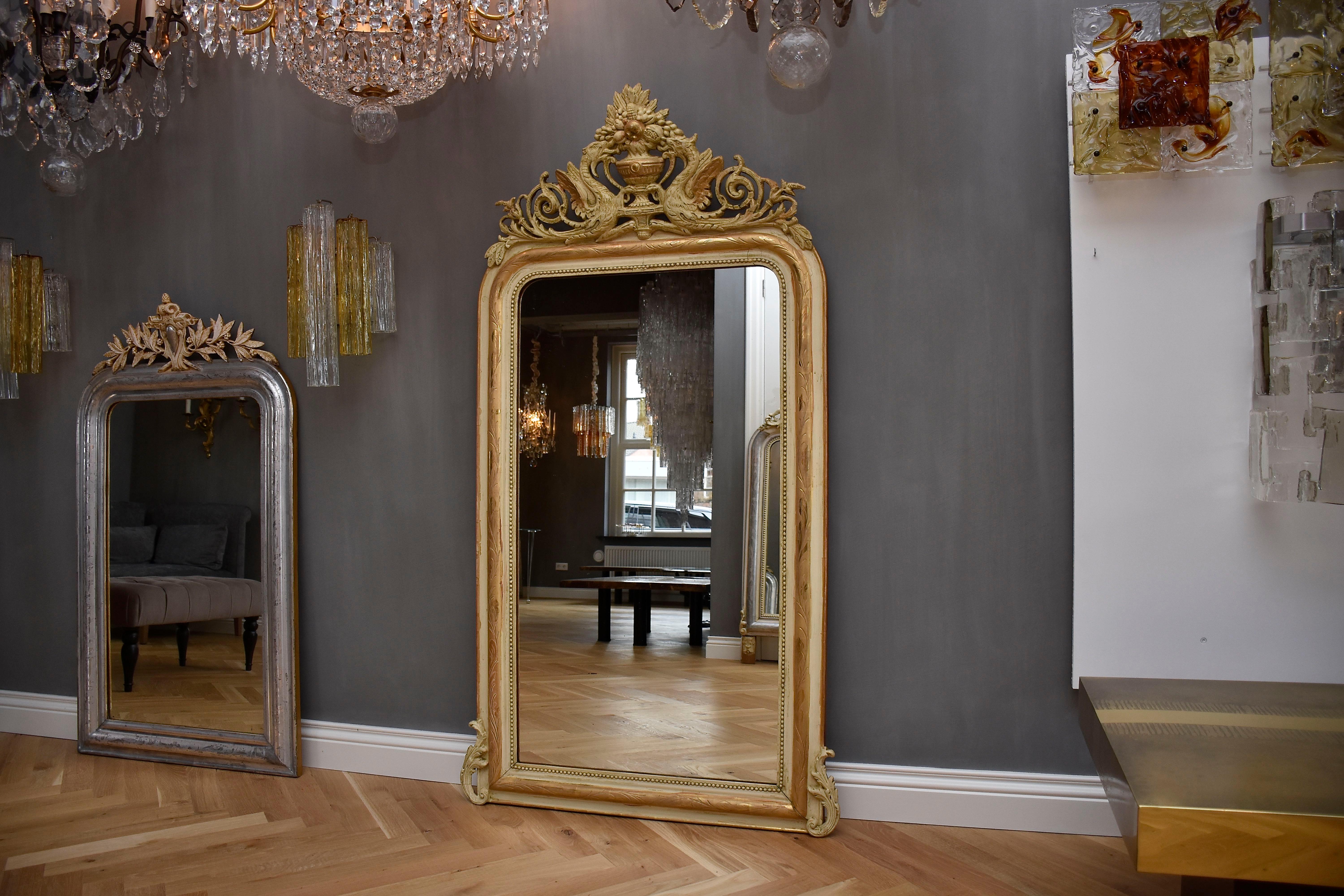 Un élégant miroir français ancien Louis Philippe avec une crête impressionnante.
L'écusson ajouré représente deux dragons prenant des fruits dans une corbeille. 
Le cadre a une couleur crème d'origine et une dorure à la feuille d'or. Il est gravé de