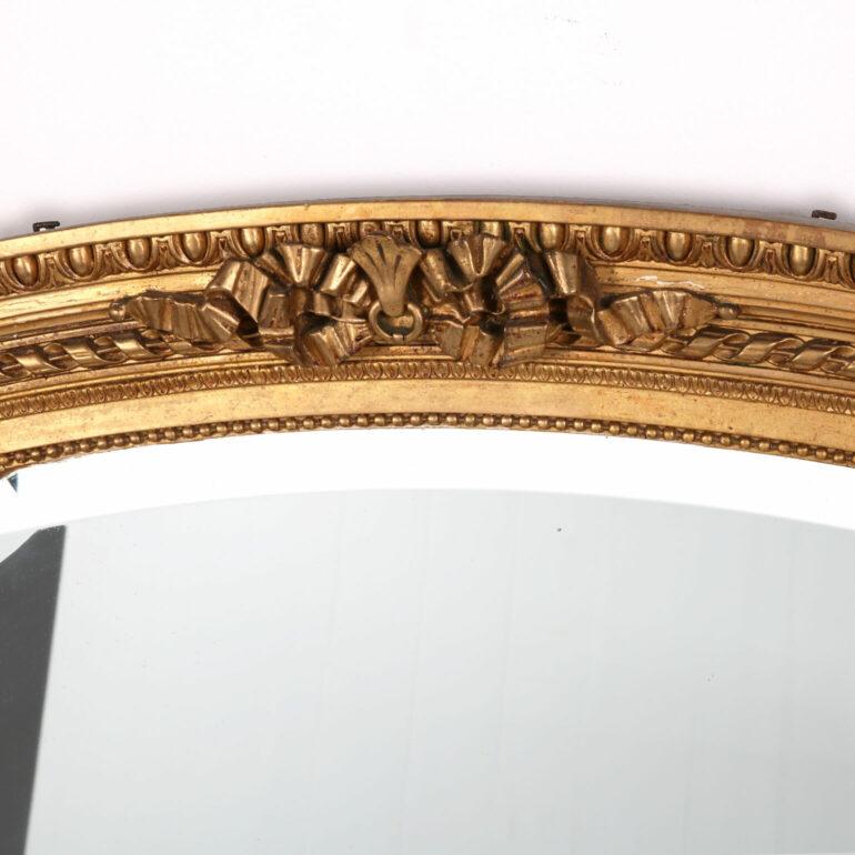 A late 19th century giltwood mirror of fine quality and proportions. The beveled mirror is set within a hand carved, moulded giltwood frame with beaded row borders around. Surmounted with a centred crest composition of a scrolling ribbon detail, all