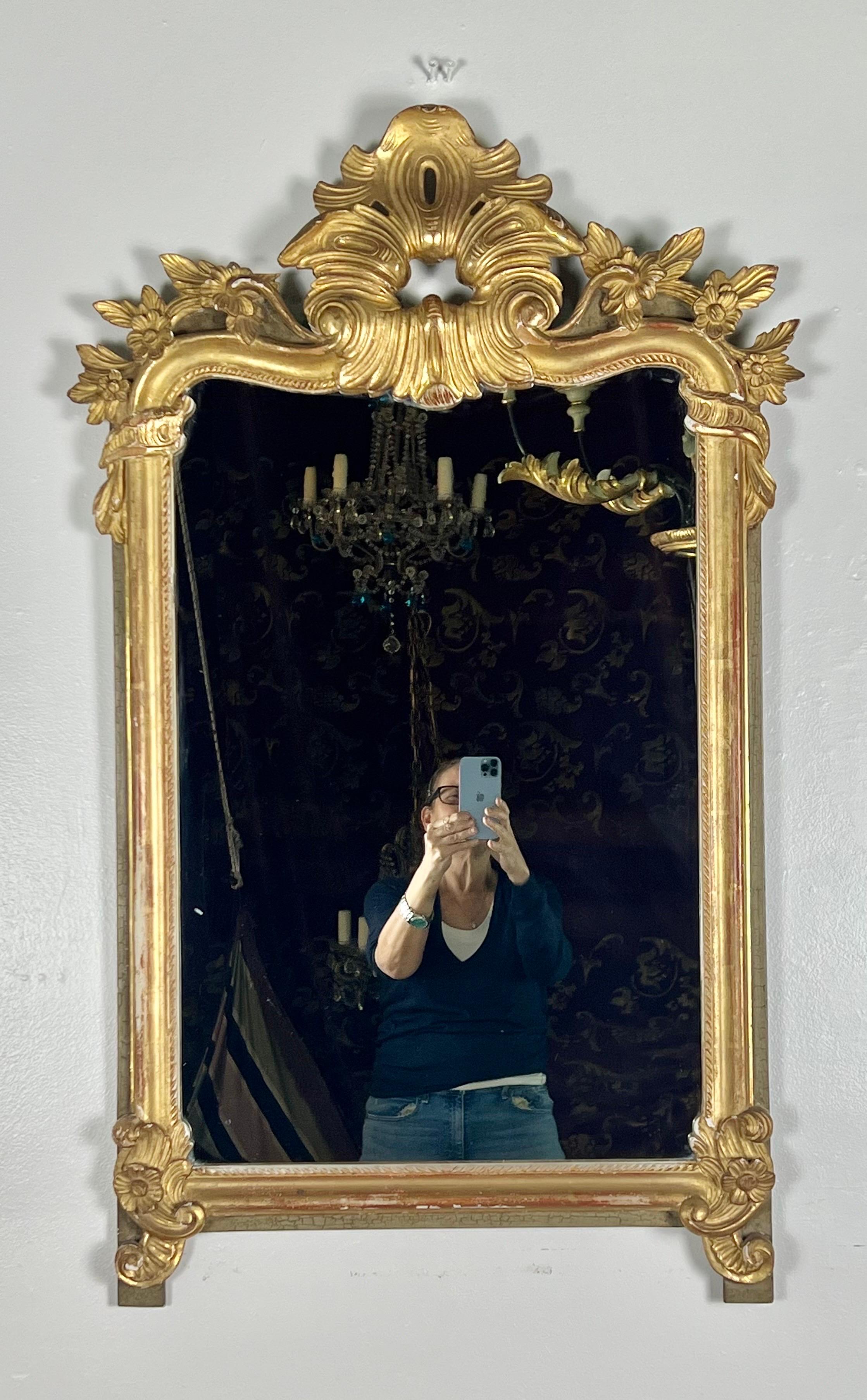 Miroir en bois doré français du 19e siècle.  Le miroir est magnifiquement sculpté de minuscules fleurs encadrant un motif central inspiré d'une feuille d'acanthe.  Le miroir est fini en feuille d'or 22K.  Le miroir repose sur des pieds à feuilles