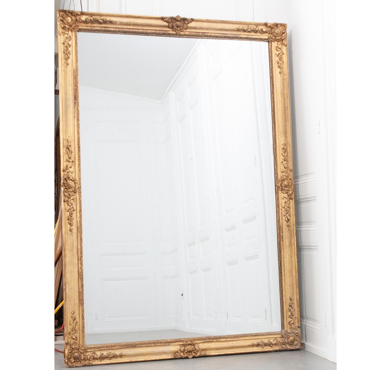 Huge French 19th century mirror with its original mirror plate. Both the frame and mirror show age. The gold gilt frame has carvings on all four corners as well as the center of each side.