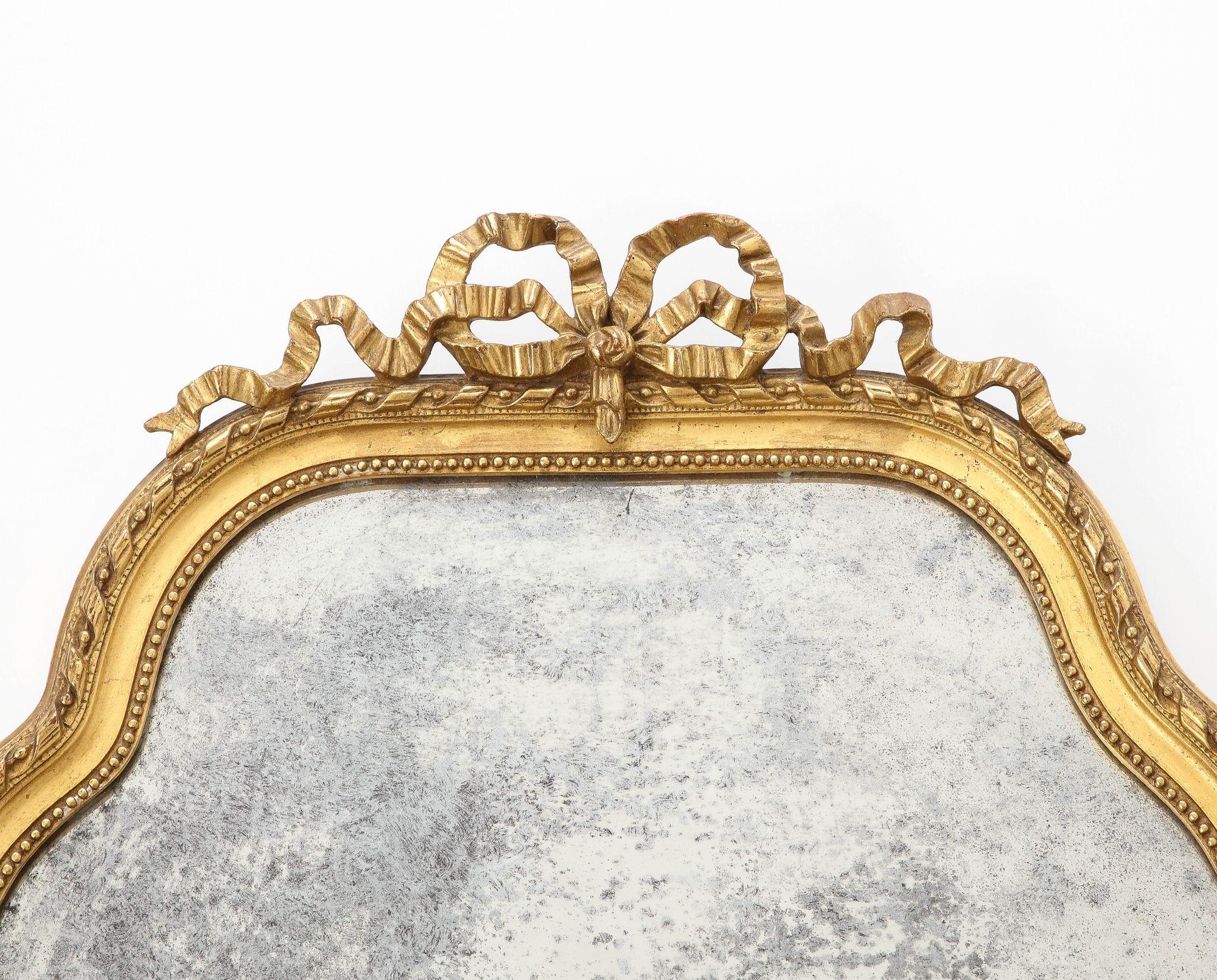 A 19th century small giltwood mirror with a bow crown. The lozenge-shaped wood frame features a beaded border. The glass plate has a heavy patina, highly desired by collectors. The back of the frame features a label from Adolphe Braun. Braun was a