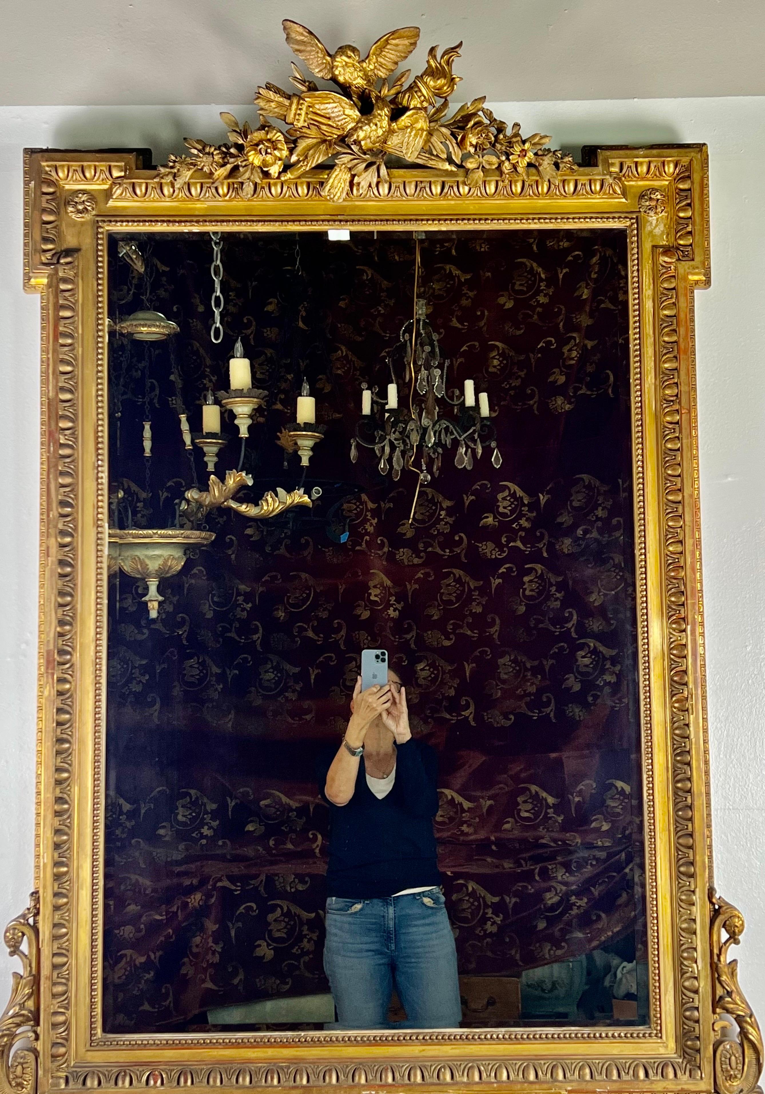 19th century French neoclassical style Giltwood mirror. The mirror is beautifully finished in 22K gold leaf. The frame is finely detailed with a pair of birds at the top with crossed torches and flowers throughout. The frame is detailed with an egg