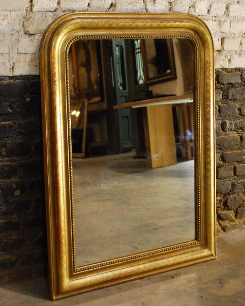 This beautiful French mirror is completely gold gilt and is made in Louis Philippe style with its typical rounded upper corners.
The mirror frame has a pearl beading surrounding the glass. The most elevated part of the frame has a classical cross