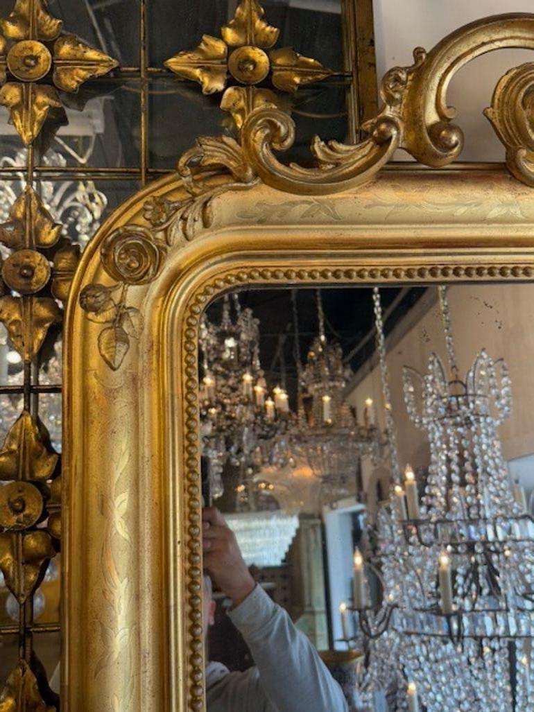 Eleva il tuo spazio con l'eleganza dello Specchio Louis Philippe del XIX secolo in legno dorato francese con un bellissimo stemma nella parte superiore. La splendida cornice a specchio riflette magnificamente la luce, creando un ambiente ampio e