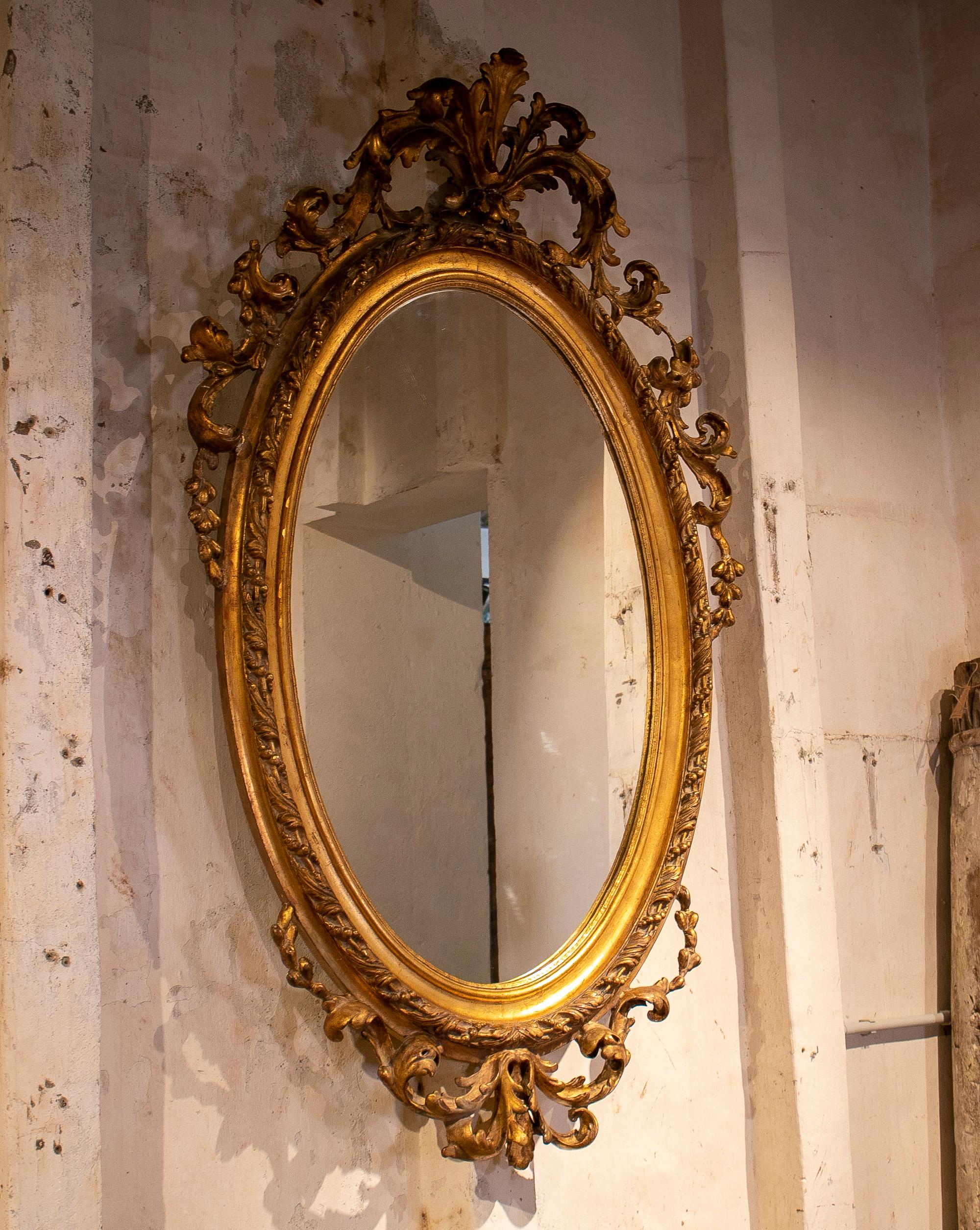 Espejo ovalado francés del siglo XIX de madera dorada con cresta, decorado con rocalla rococó del Barroco tardío.