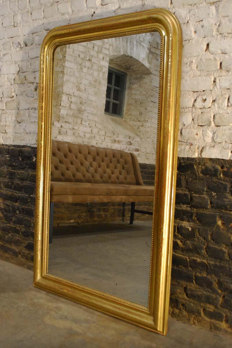 This beautiful large French mirror is completely gold leaf gilt and is made in Louis Philippe style with it's typical rounded upper corners. The mirror frame has a pearl beading surrounding the glass. The most elevated part of the frame has a