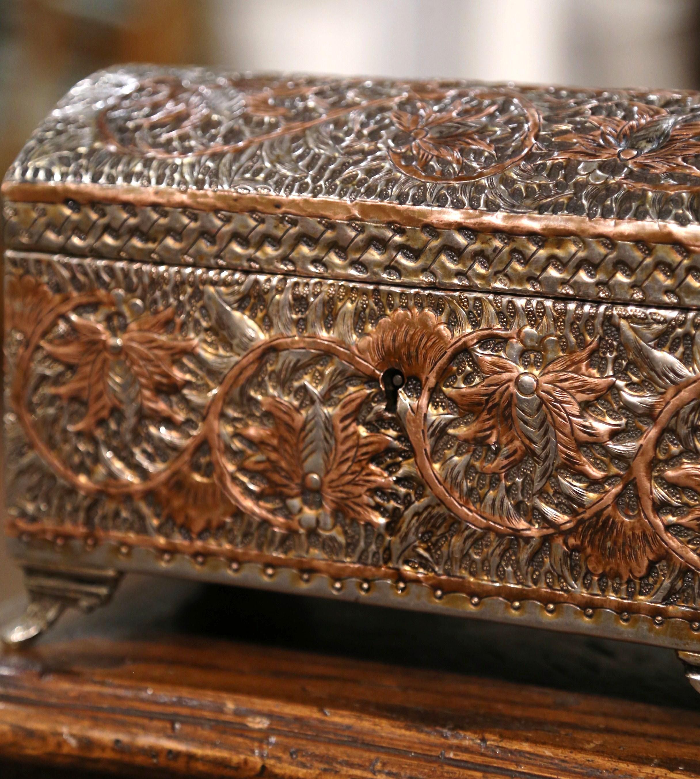 This antique patinated gilt casket was created in France, circa 1890. Built with brass and copper, the miniature trunk-shaped box with bombe top, stands on curved feet, and is embellished with intricate repousse floral and leaf motifs on all four