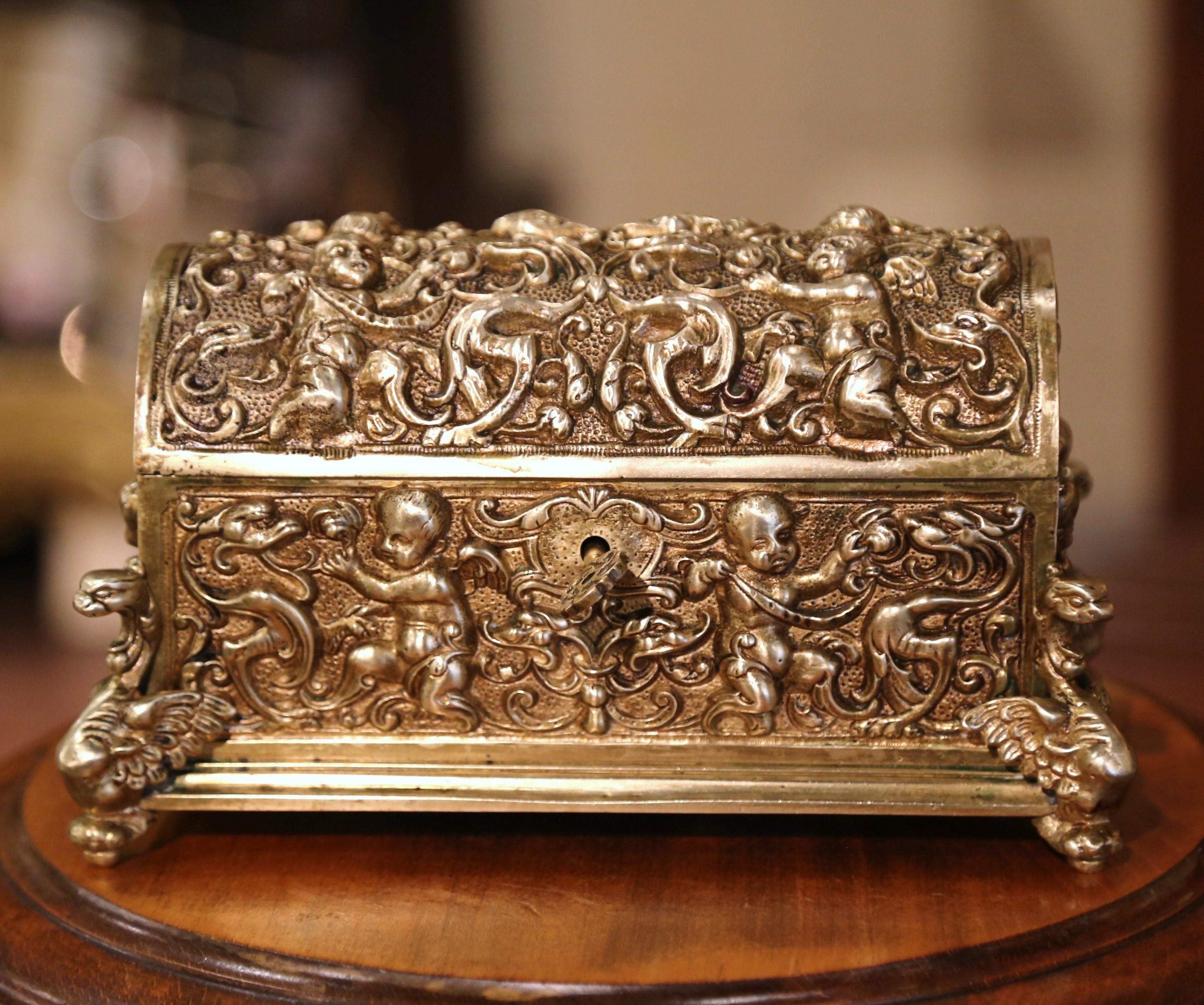 This antique gilt bronze casket was created in France, circa 1870. The miniature trunk-shaped box with bombe top, stands on gargoyle figure feet, and is embellished with intricate repousse cherub and scrolled decor on all four sides. The jewelry box