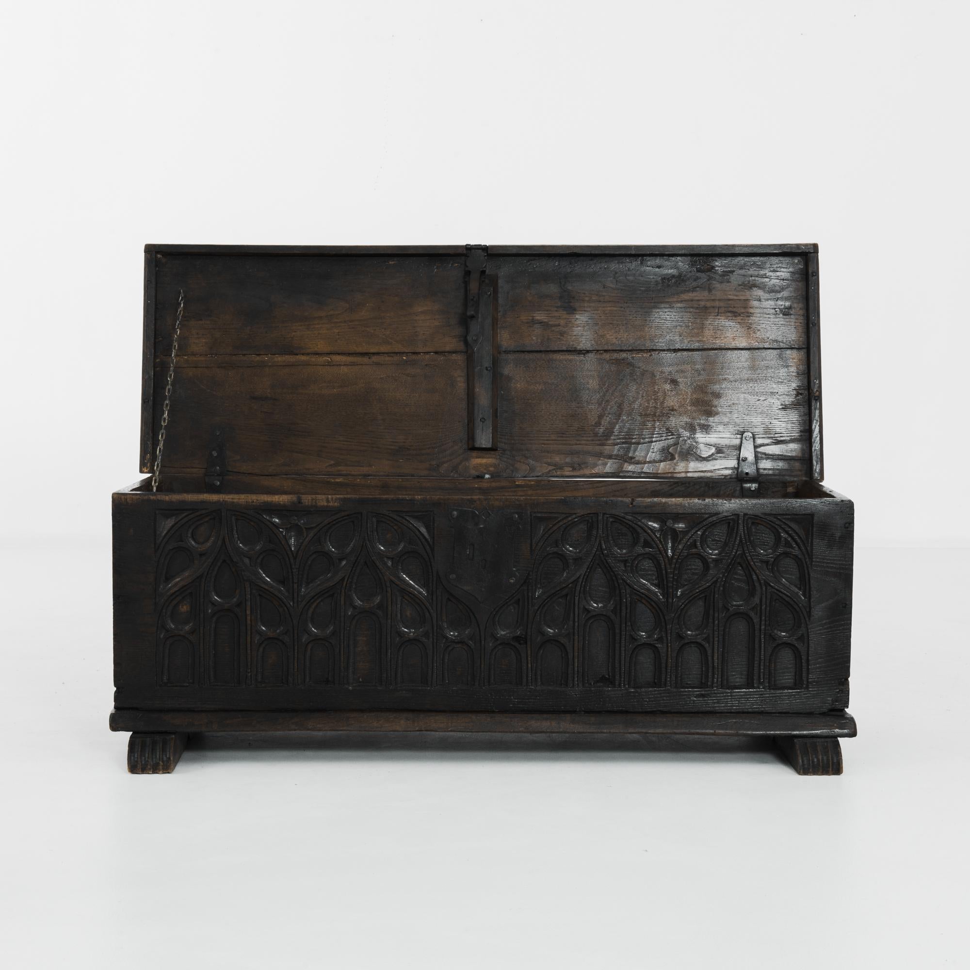 An oak trunk from 1850s France. Intertwining carved arches echo the forms of gothic tracery, lending the dark wood a Neo-Gothic aesthetic. The lid is closed with a hefty metal latch and crest shaped lock plate, a personal detail which lends this