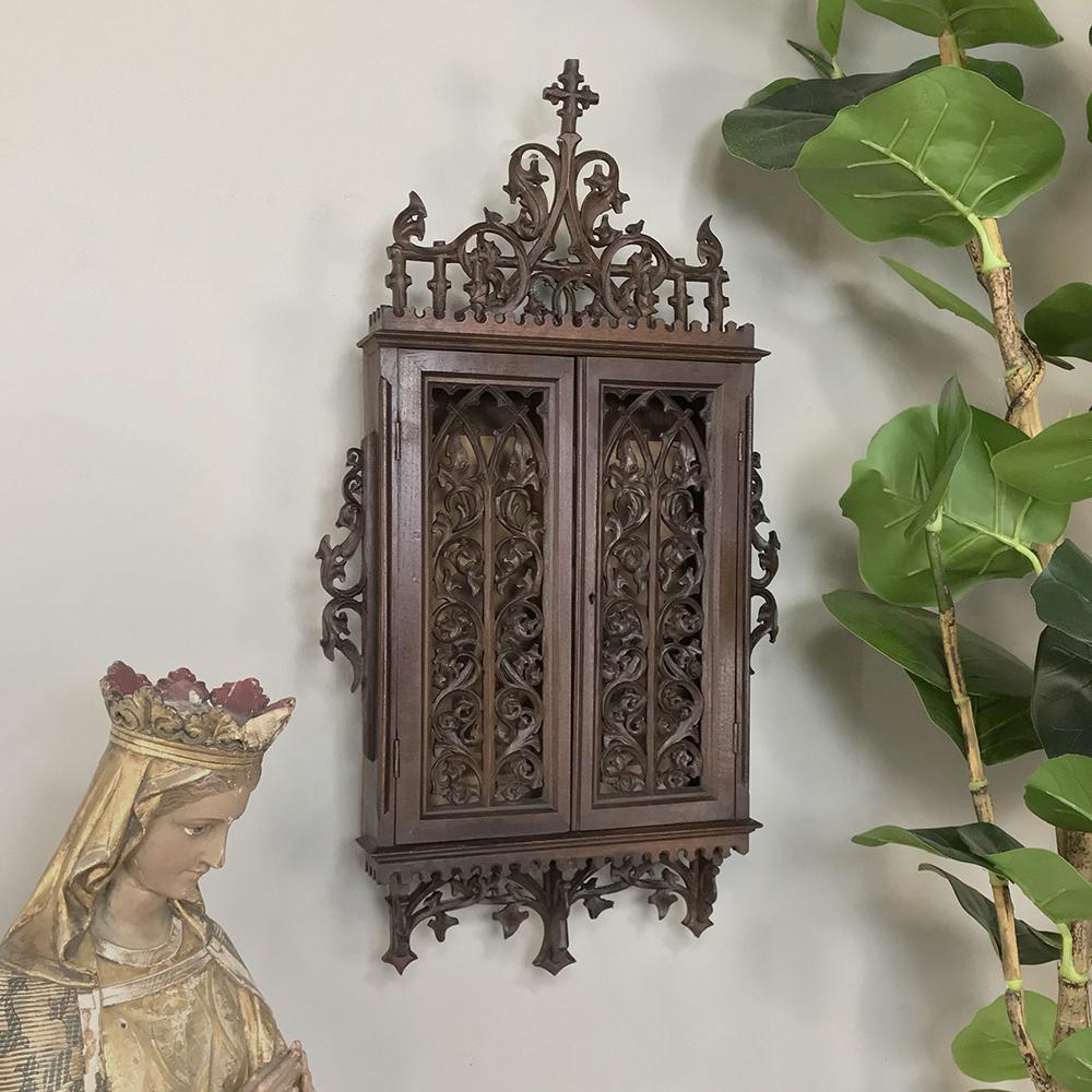 19th century French Gothic reliquary cabinet is a study in intricacy, with amazing detail sculpted from solid oak with patterns inspired by grapevines, foliates, and wood intertwined with a cross above and inverted fleurs de lys below. Designed as a
