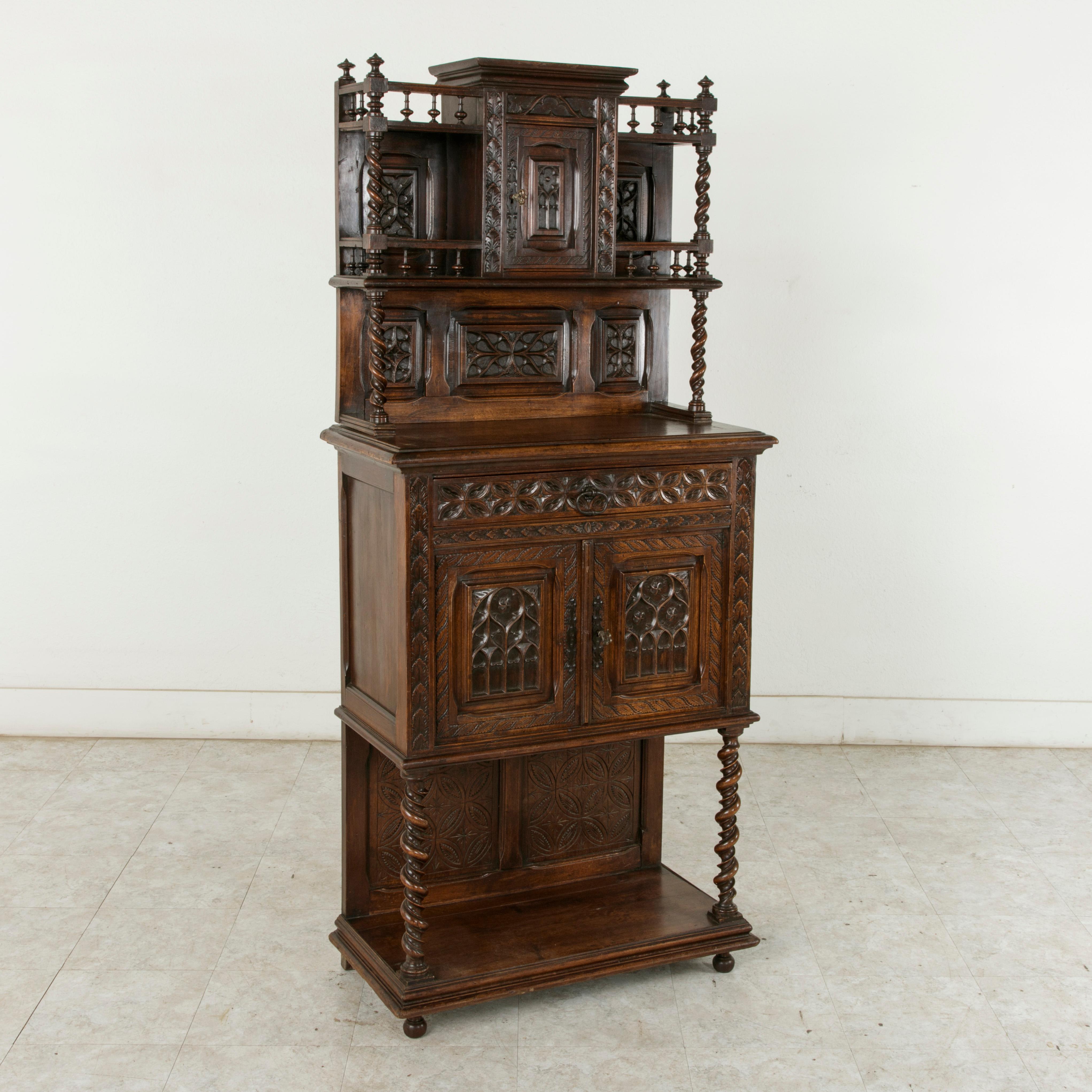 This late 19th century French Gothic style oak and walnut credenza features intricately hand carved Gothic motifs on all forward facing panels and double spiraled barley twist columns that support its many levels. At counter height is a single