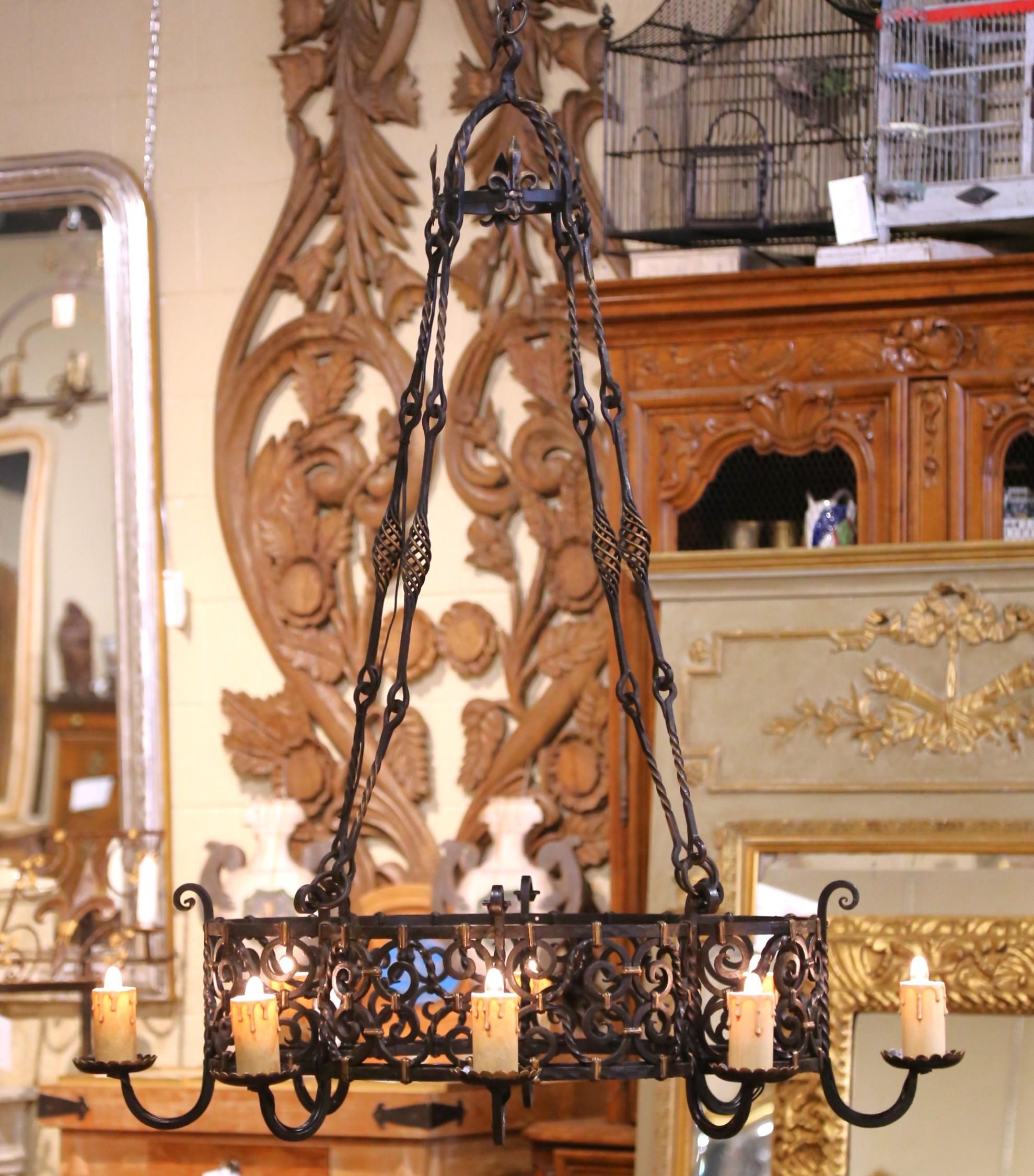 Realizzato in Francia intorno al 1880, questo imponente lampadario in stile gotico presenta un'audace cornice rettangolare ornata da intricate volute e dettagli forgiati a mano. La struttura è sostenuta da quattro supporti in ferro ritorto con