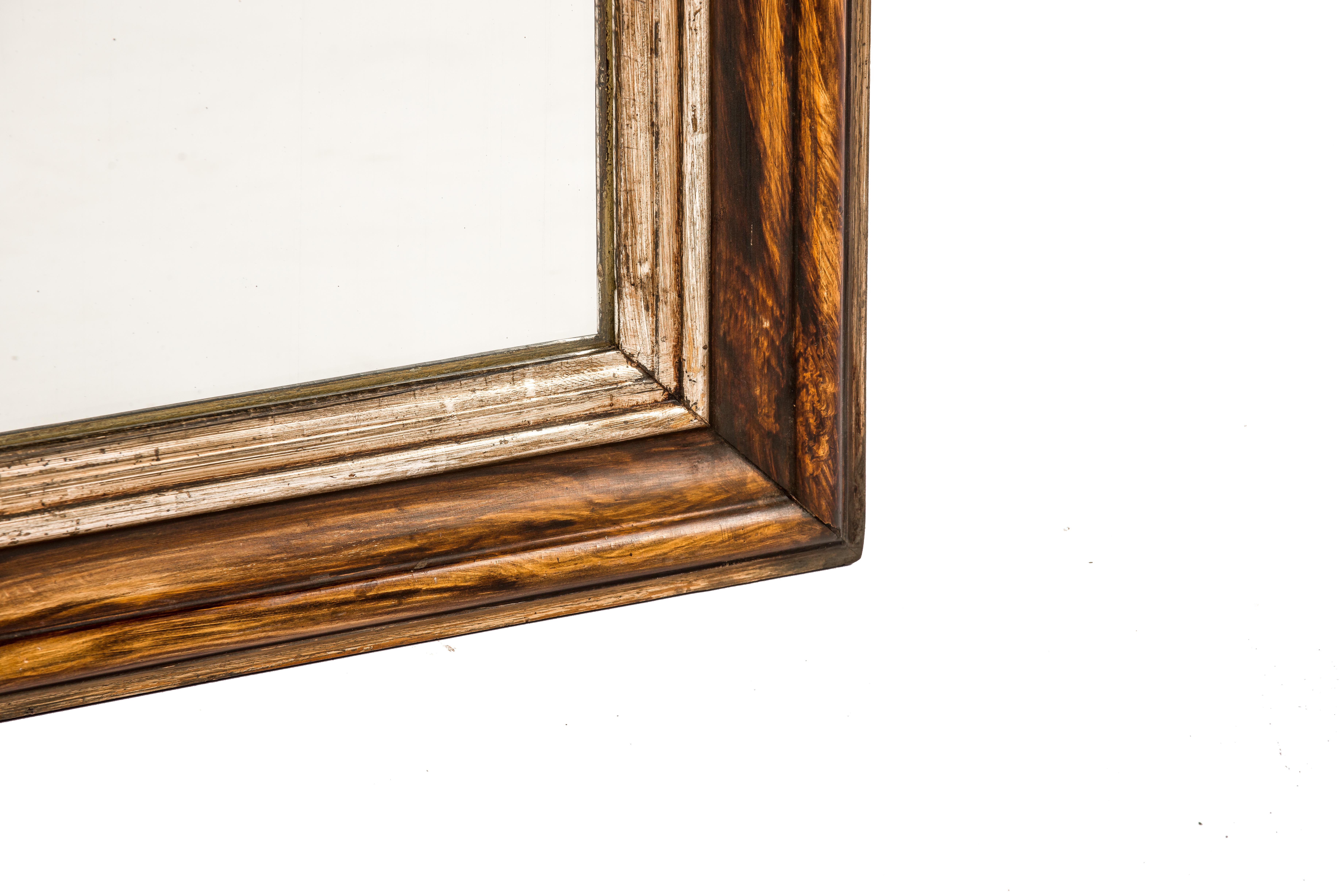 This Louis Philippe mirror was made in Northern France in the late 1800s. The mirror has a solid pine frame that was smoothened with gesso. The mirror frame is painted to resemble rosewood with a beautiful grain pattern. The most elevated part of