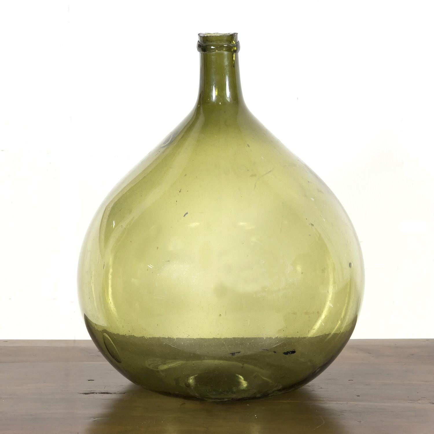 Magnifique bouteille en verre vert soufflé à la bouche ou Dame Jeanne, vers les années 1880, de forme bulbeuse et de couleur verte vive, avec des bulles visibles et sans coutures, ce qui indique qu'elle a été soufflée à la main plutôt que fabriquée