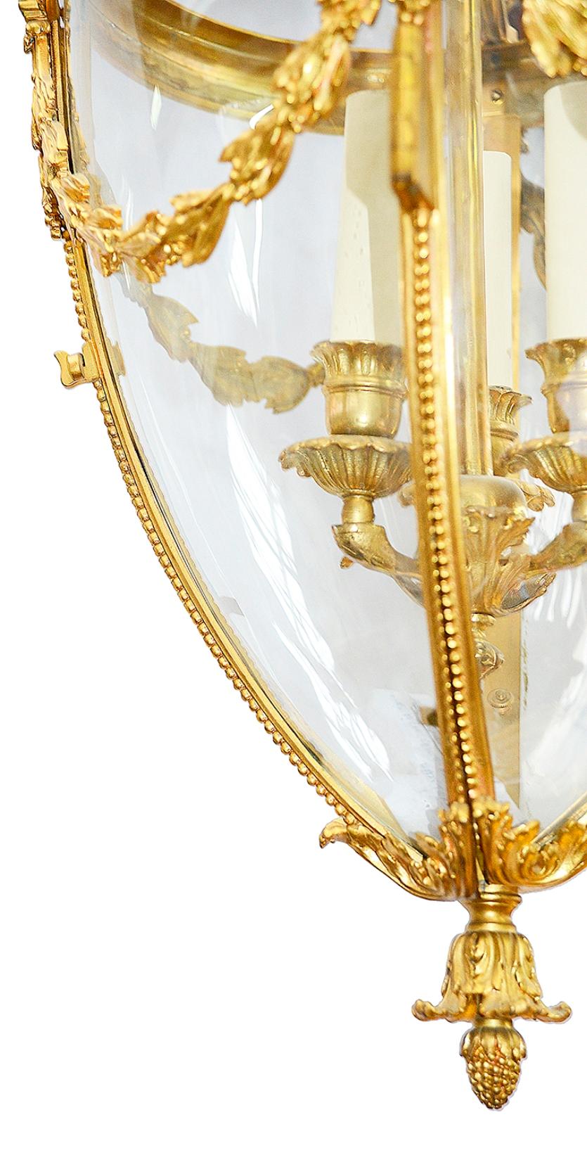 A very good quality late 19th century French gilded ormolu hall lantern, having four out swept supports from the top, foliate finials and swags to the bowed glass panels, a hinged door opening to access the three branch candle sconces, beaded