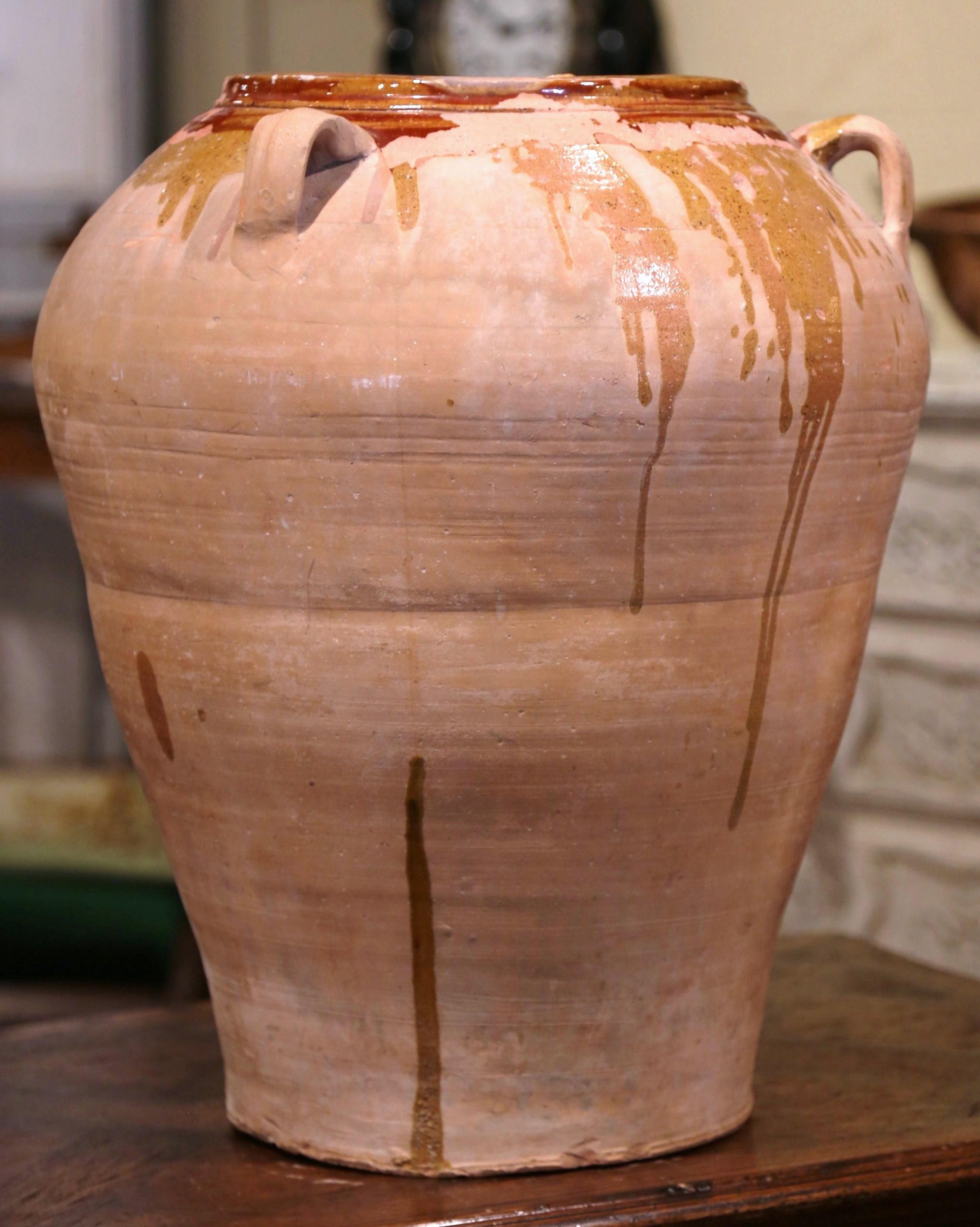 This large, antique earthenware jar was created in Southern France, circa 1870. Made of blond clay, the terracotta pot is round in shape with a tapered base and features three handles at the top; the olive jar is embellished with a brown beige glaze