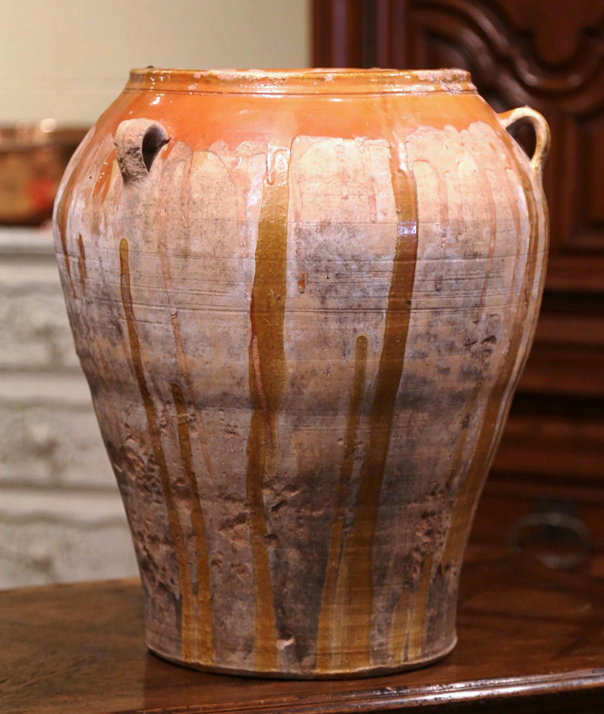 This large, antique earthenware jar was created in Southern France, circa 1870. Made of blond clay, the terracotta pot is round in shape with a tapered base and features with three handles at the top; the olive jar is embellished with a light brown