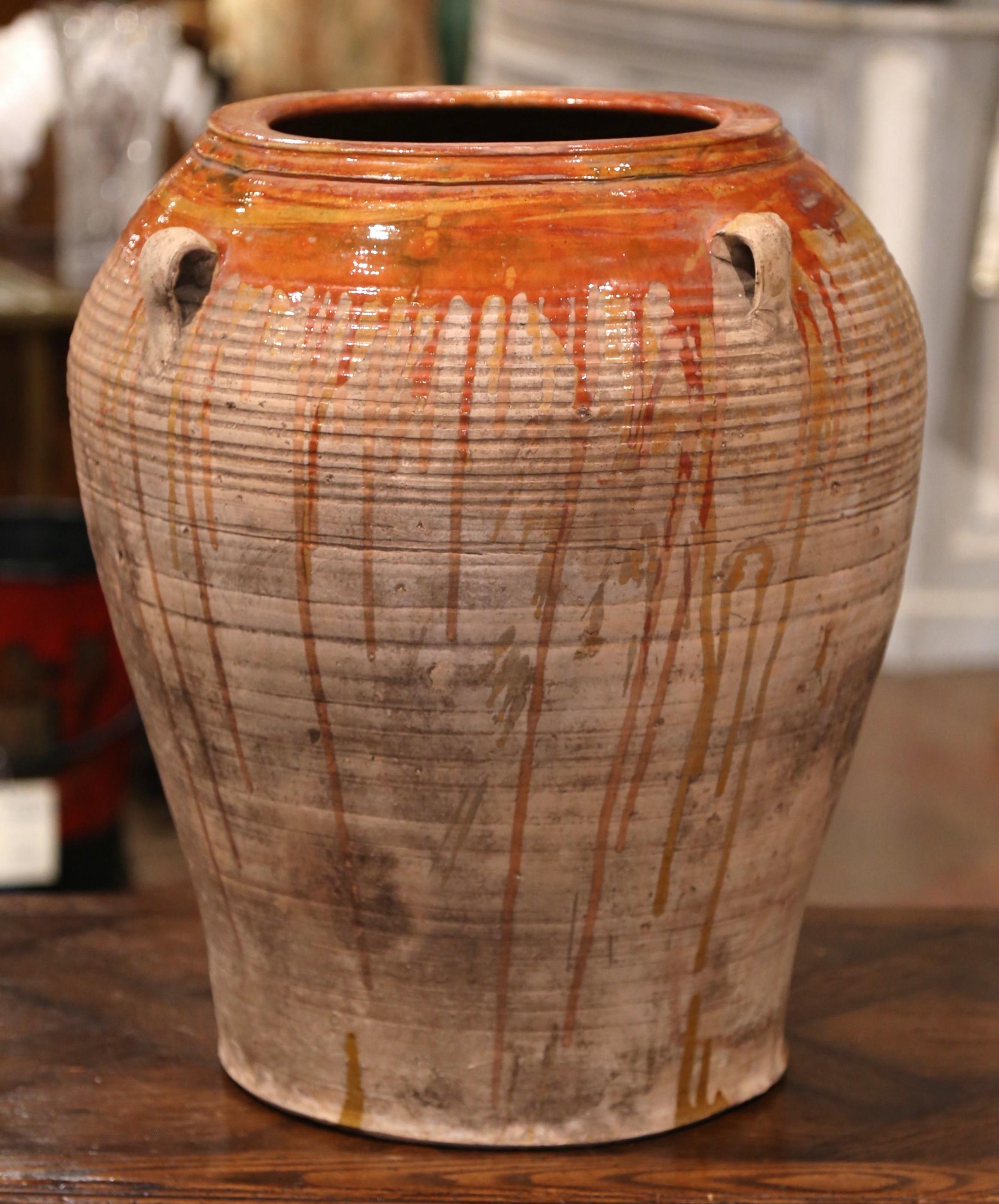 This large, antique earthenware jar was hand made in Southern France, circa 1870. Built of blond clay, the terracotta pot is round in shape with a tapered base decorated with four handles at the top; the olive jar is embellished with a mustard glaze