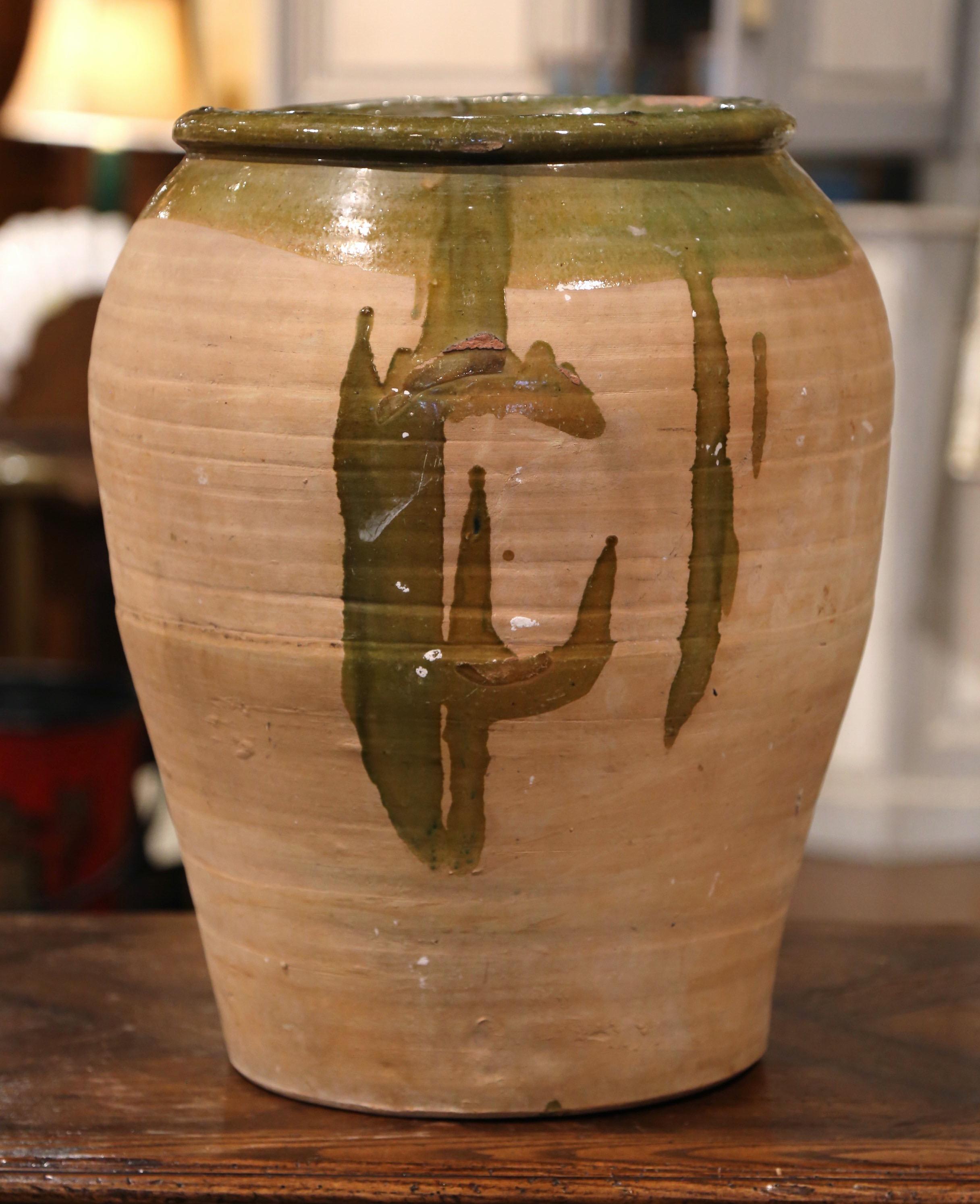This large, antique earthenware jar was created in Southern France, circa 1870. Made of blond clay, the terracotta pot is round in shape with a tapered base; the olive jar is embellished with the traditional green glaze around the neck and rim with