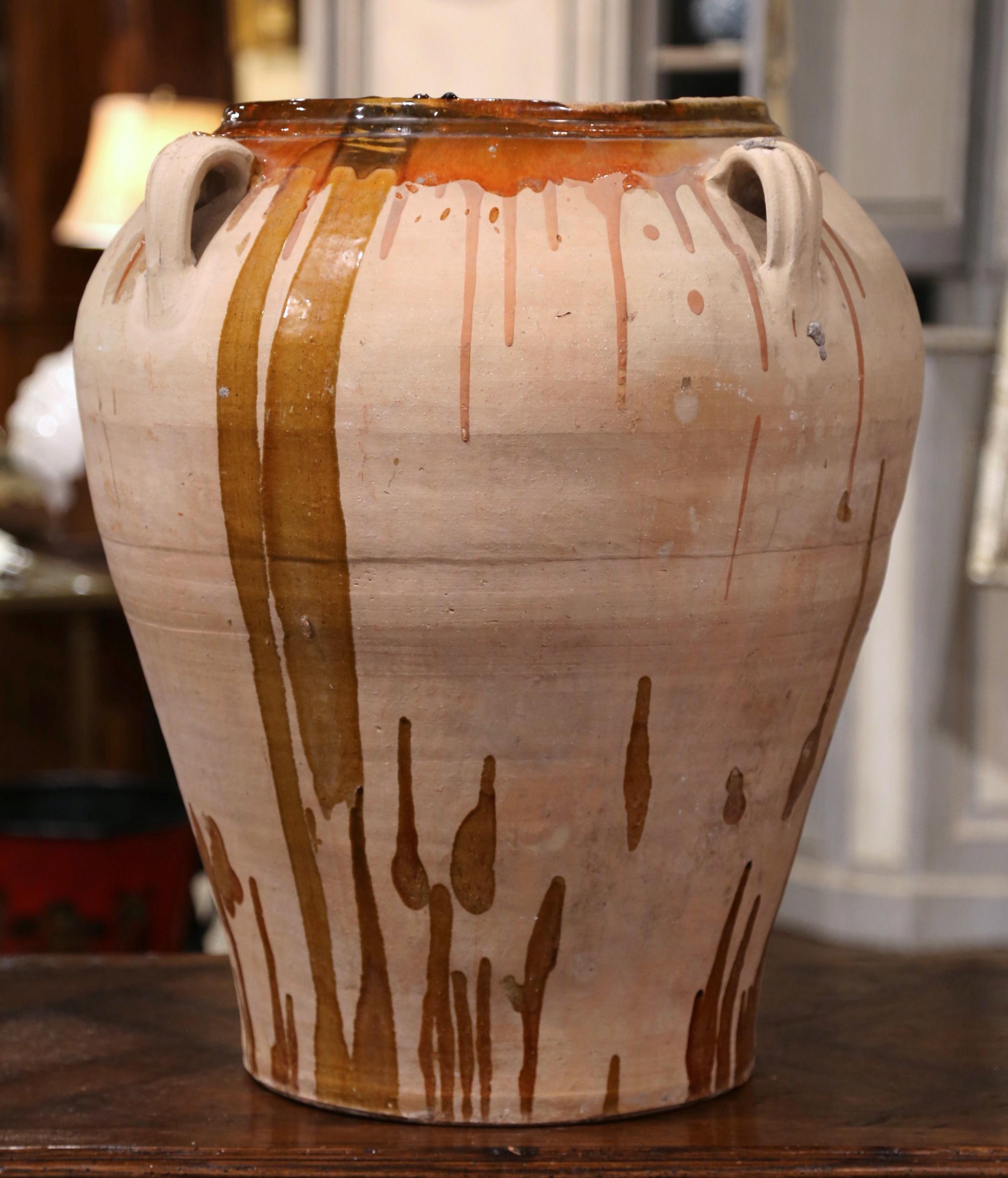 This large, antique earthenware jar was created in Southern France, circa 1870, made of blond clay and round in shape with a tapered base, the terracotta pot features four handles at the top. The jar is decorated with a brown beige glaze around the
