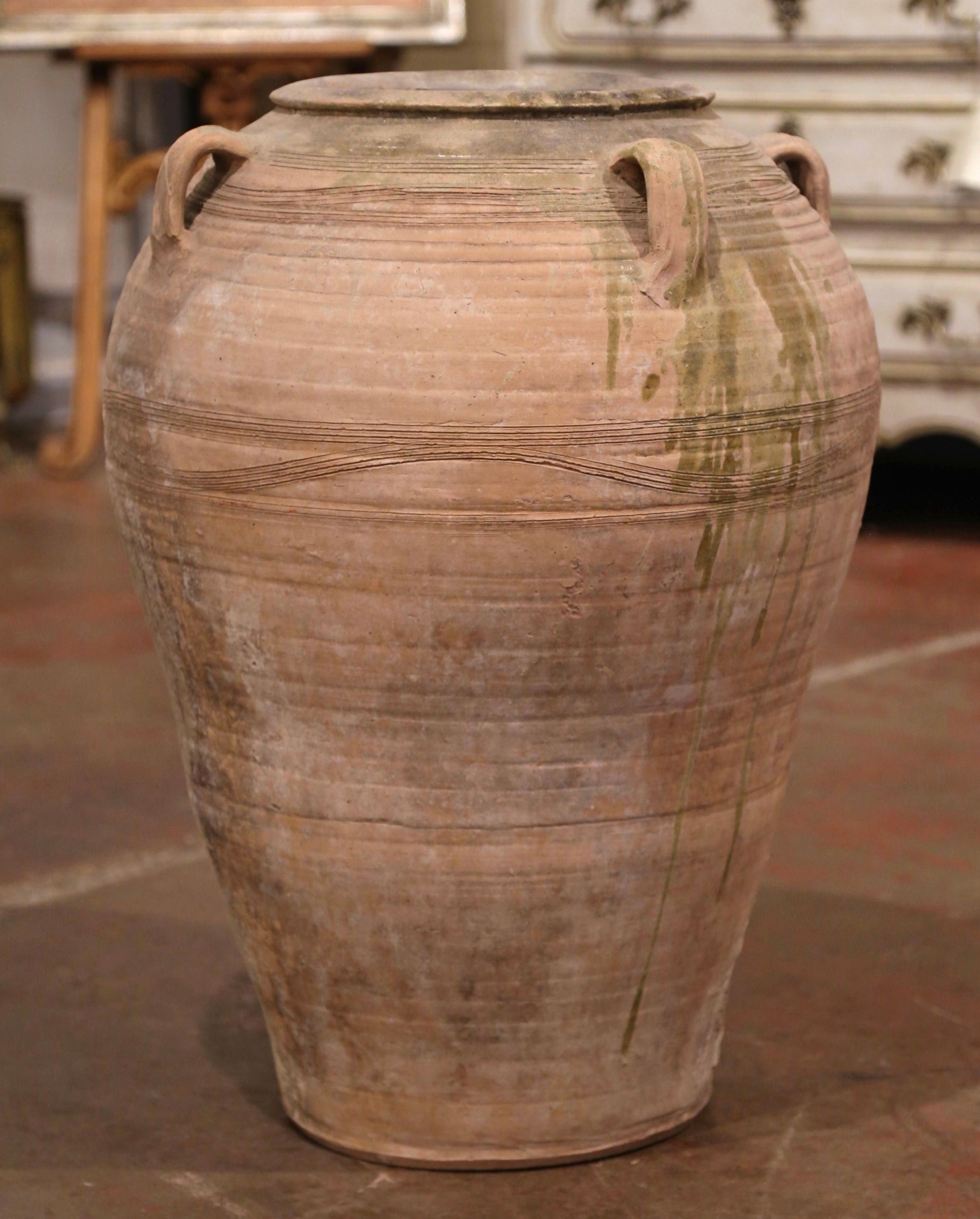 This large, antique earthenware jar was created in Southern France, circa 1870. Made of blond clay, the tall vessel is round in shape with a tapered base and decorated with four handles at the top; the olive jar is embellished with a terracotta