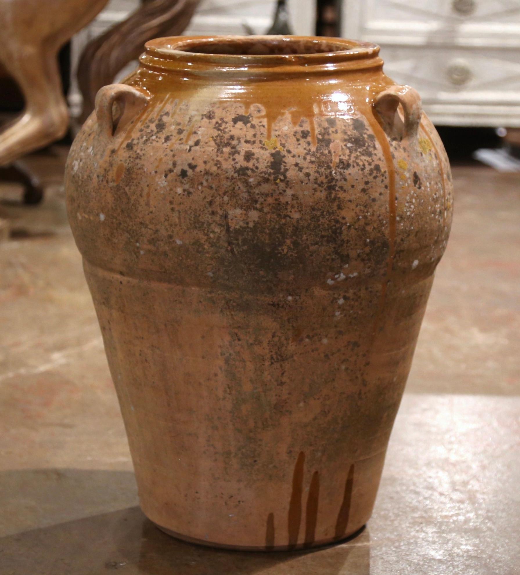 This large, antique earthenware jar was created in Southern France, circa 1870. Made of blond clay, the terracotta pot is round in shape with a tapered base and features a spout, and three handles at the top; the olive jar is embellished with a