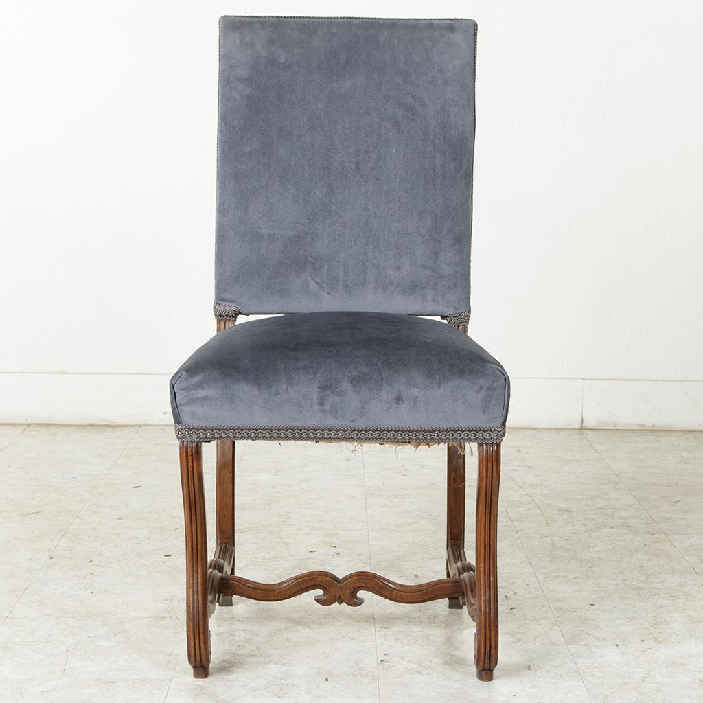 This late 19th century French Louis XIV style mutton leg side chair features hand carved fluted curved legs of solid walnut finished with scrolled feet. An H-stretcher joins the legs providing stability. The chair is upholstered in a blue velvet. An
