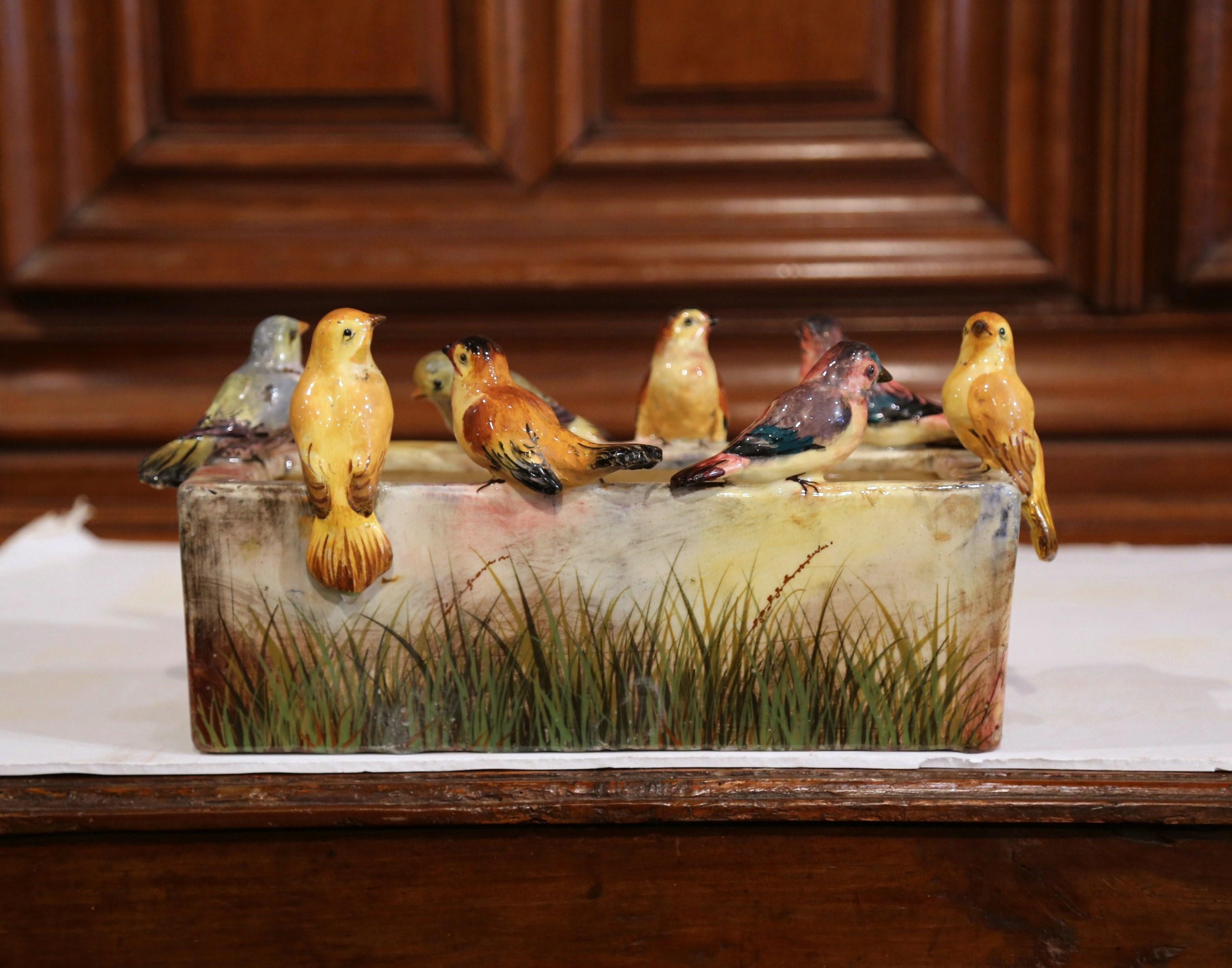 This large colorful, antique, majolica jardinière in the manner of Massier was crafted in Vallauris, France, circa 1880. The playful, rectangular planter is topped on the perimeter with seven, high-relief bird figures embellished by green grass and