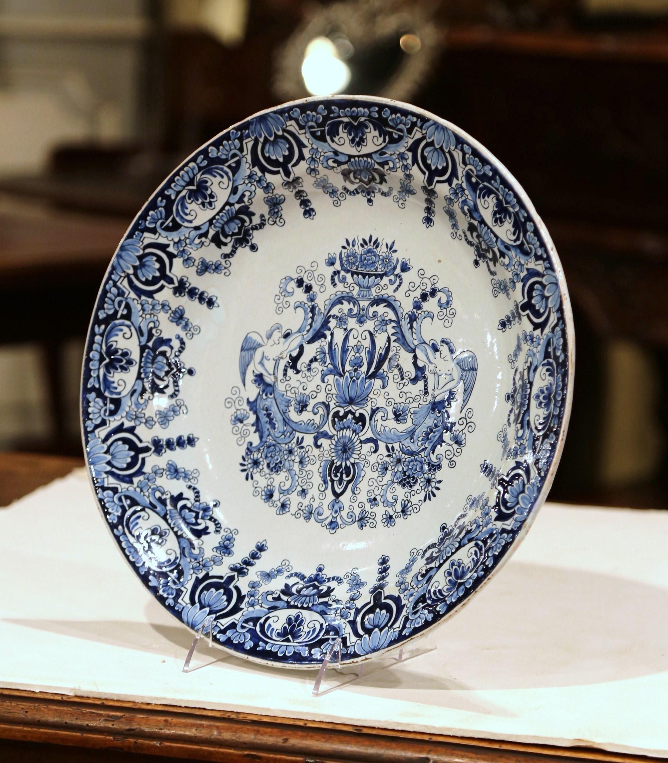 Decorate a wall or a shelf with this elegant, antique ceramic platter. Created in Bourges, France circa 1870, the ornate wall plate features hand painted blue and white floral motifs. The large ceramic plate is decorated with a center crest flanked