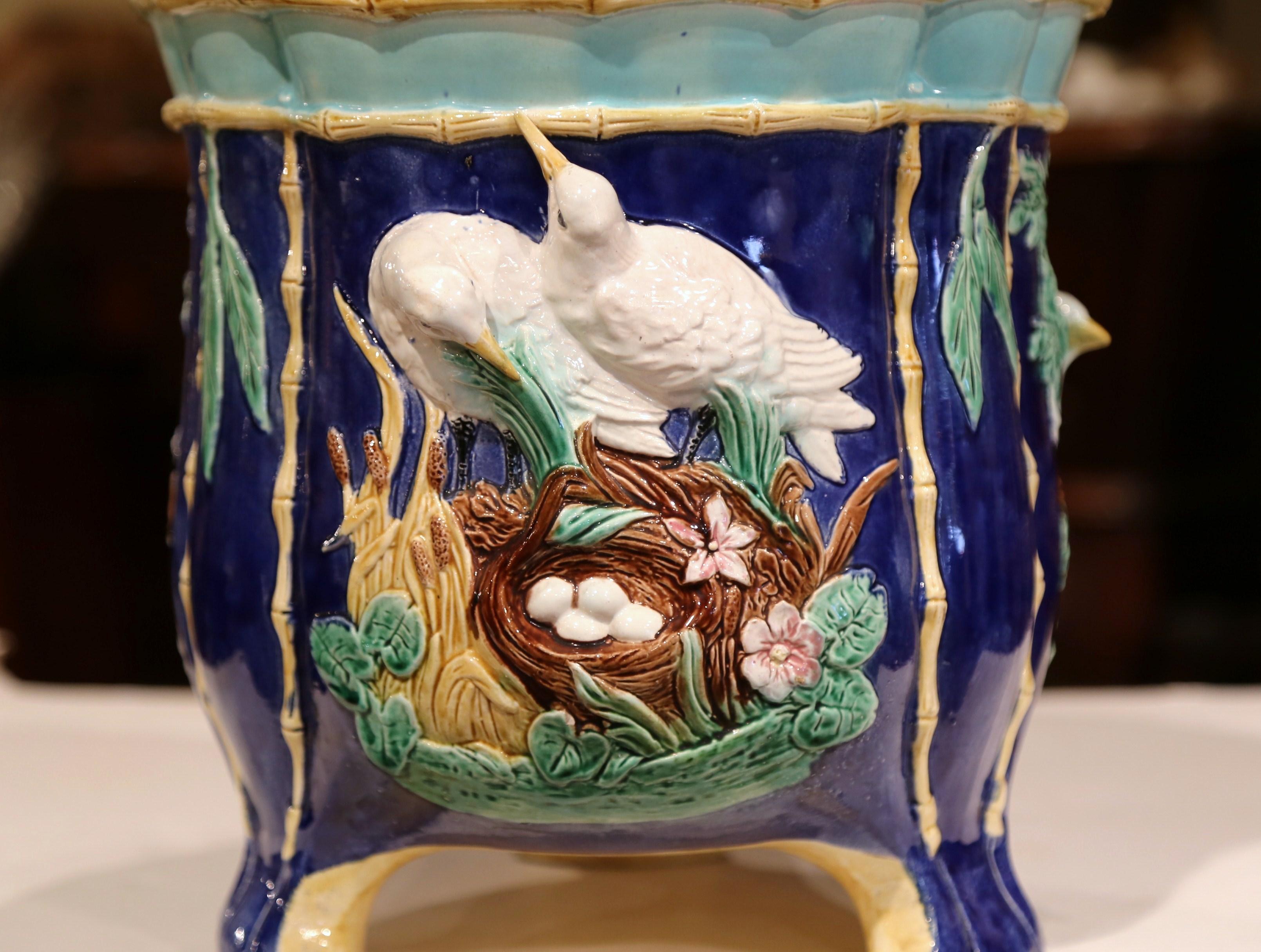 Decorate a tabletop with this colorful, antique Majolica planter. Sculpted in France circa 1870, this round cache pot features bird and foliage decorations in high relief. The porcelain vase has a scalloped edge, a raised base, and faux bamboo