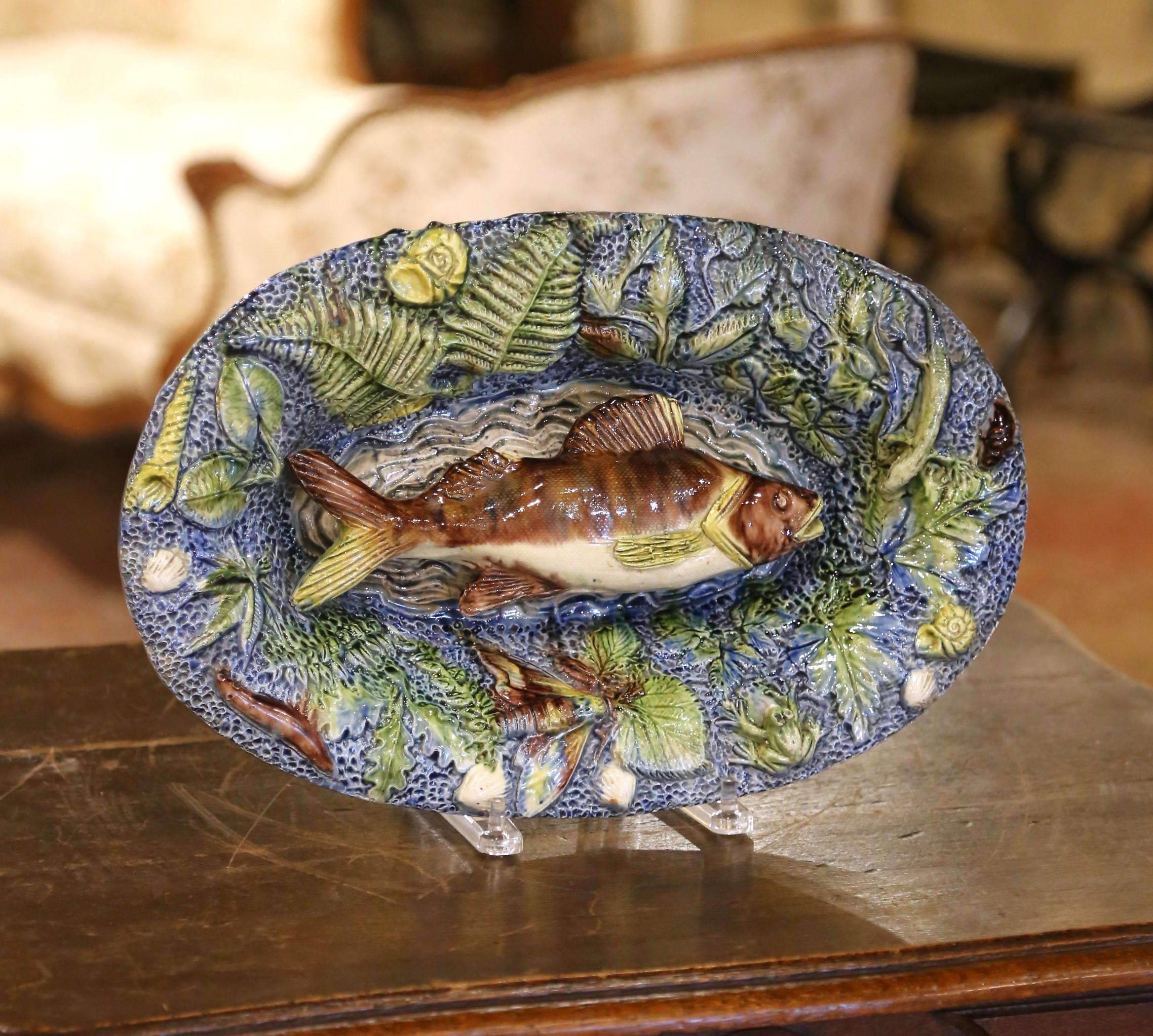 Vive et sculpturale, cette assiette ancienne en majolique de style Palissy a été fabriquée en France vers 1880 et illustre la tradition naturaliste inspirée par Bernard Palissy. Modelé en haut-relief, le plat ovale est centré sur un grand poisson
