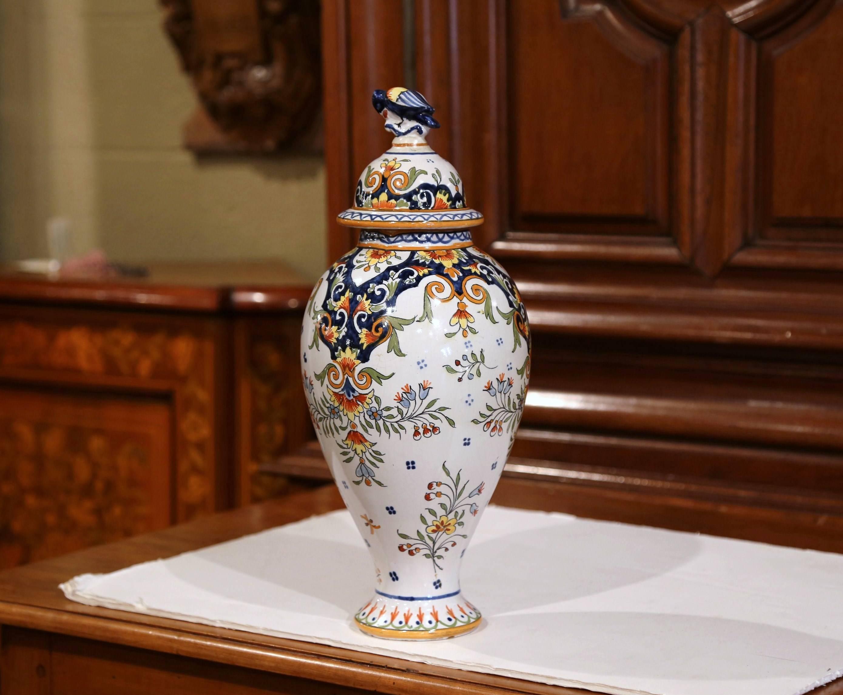 This elegant antique vase was crafted in Normandy, circa 1880. The ceramic, rounded potiche features hand painted flower decor in a traditional blue, white and yellow palette. The lid of the porcelain vase is topped with a small bird figurine. The