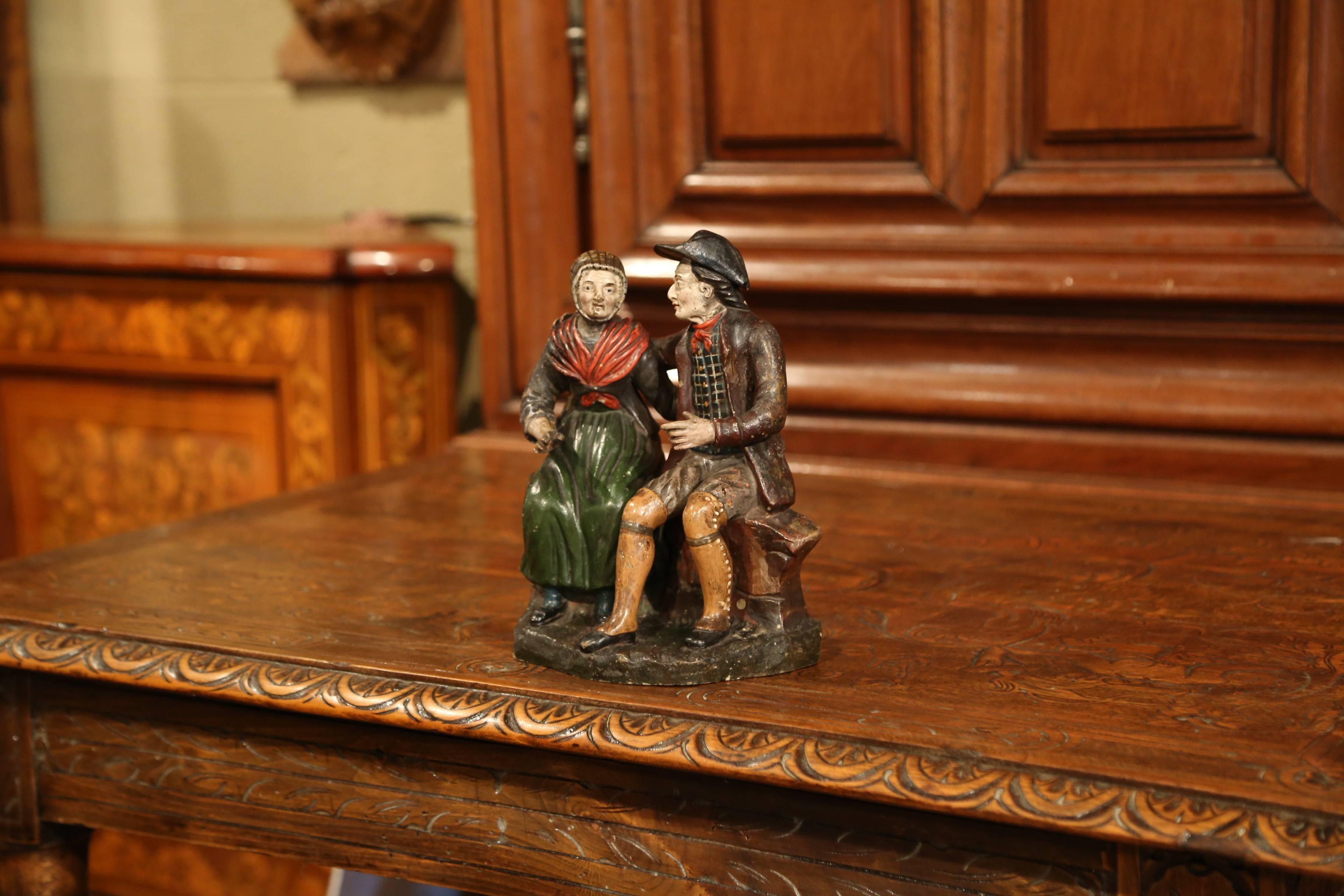 Placez cette sculpture ancienne en terre cuite colorée sur une étagère dans votre salle familiale. Fabriquée vers 1920, cette pièce en céramique représente un couple âgé assis sur un banc et se tenant dans les bras. Excellent état avec de riches